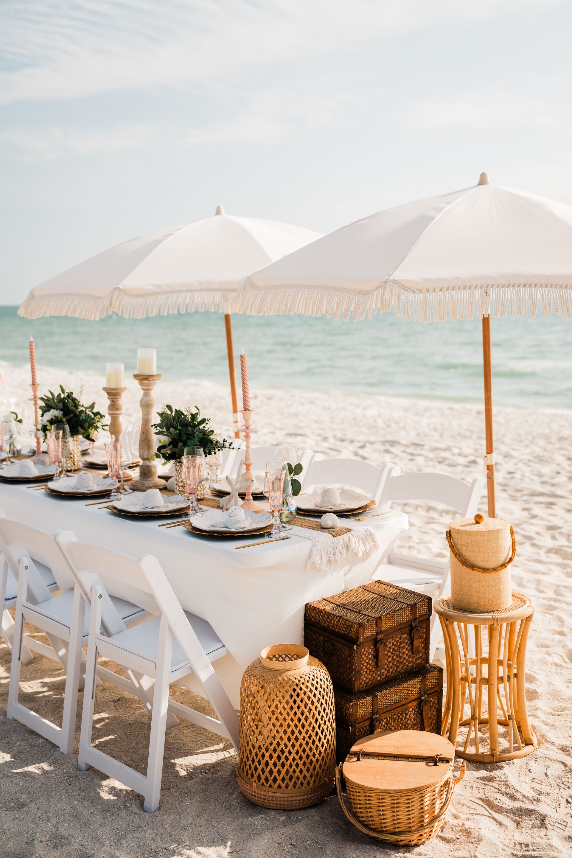 Beachside table setting with white umbrellas, ocean view, and wicker accents.