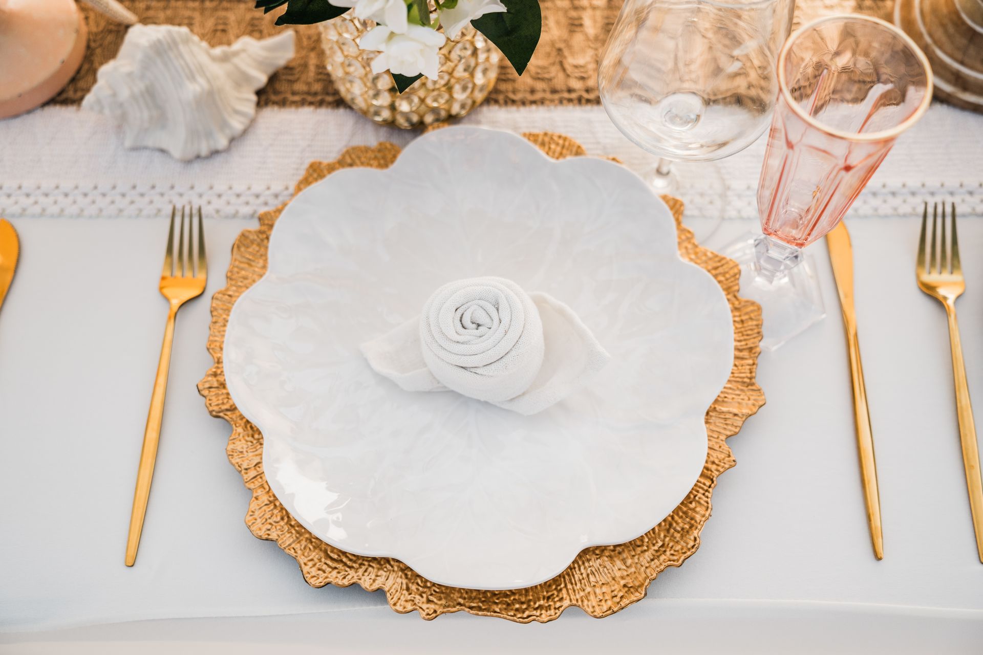 Elegant table setting with gold flatware, white plate with napkin, and a gold charger.