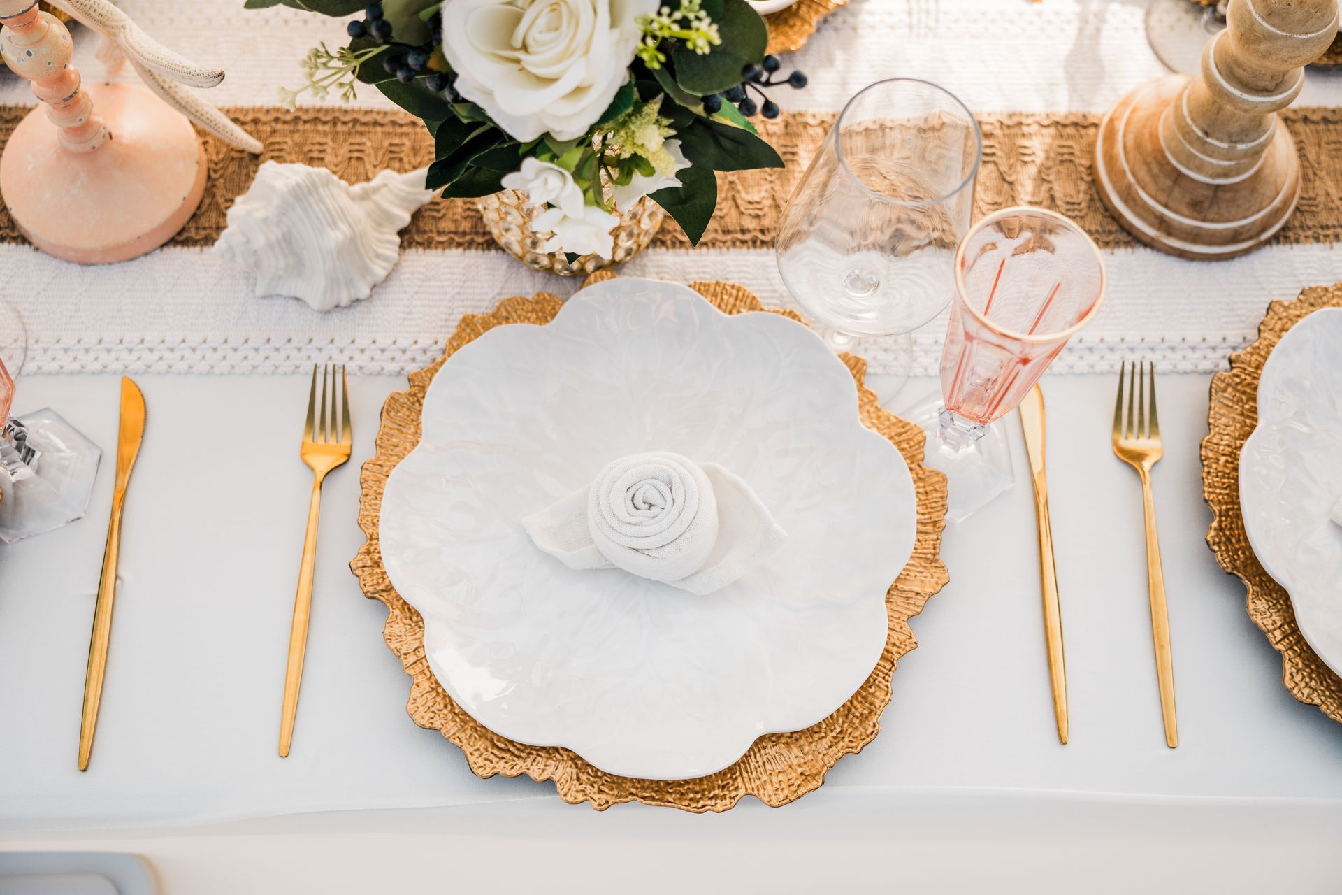 Elegant table setting with gold accents, white plates, and floral centerpiece.