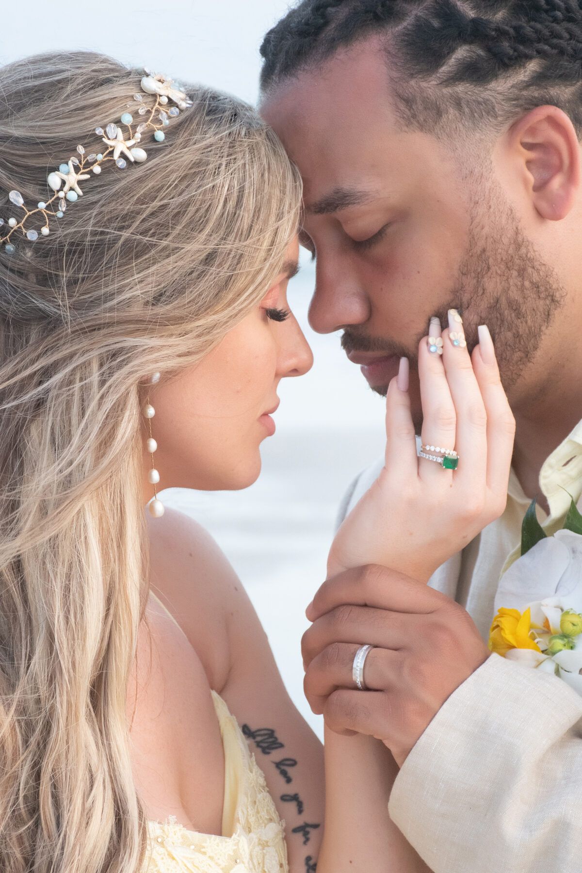 Couple embracing on a beach; woman touching man's face, both wearing rings.