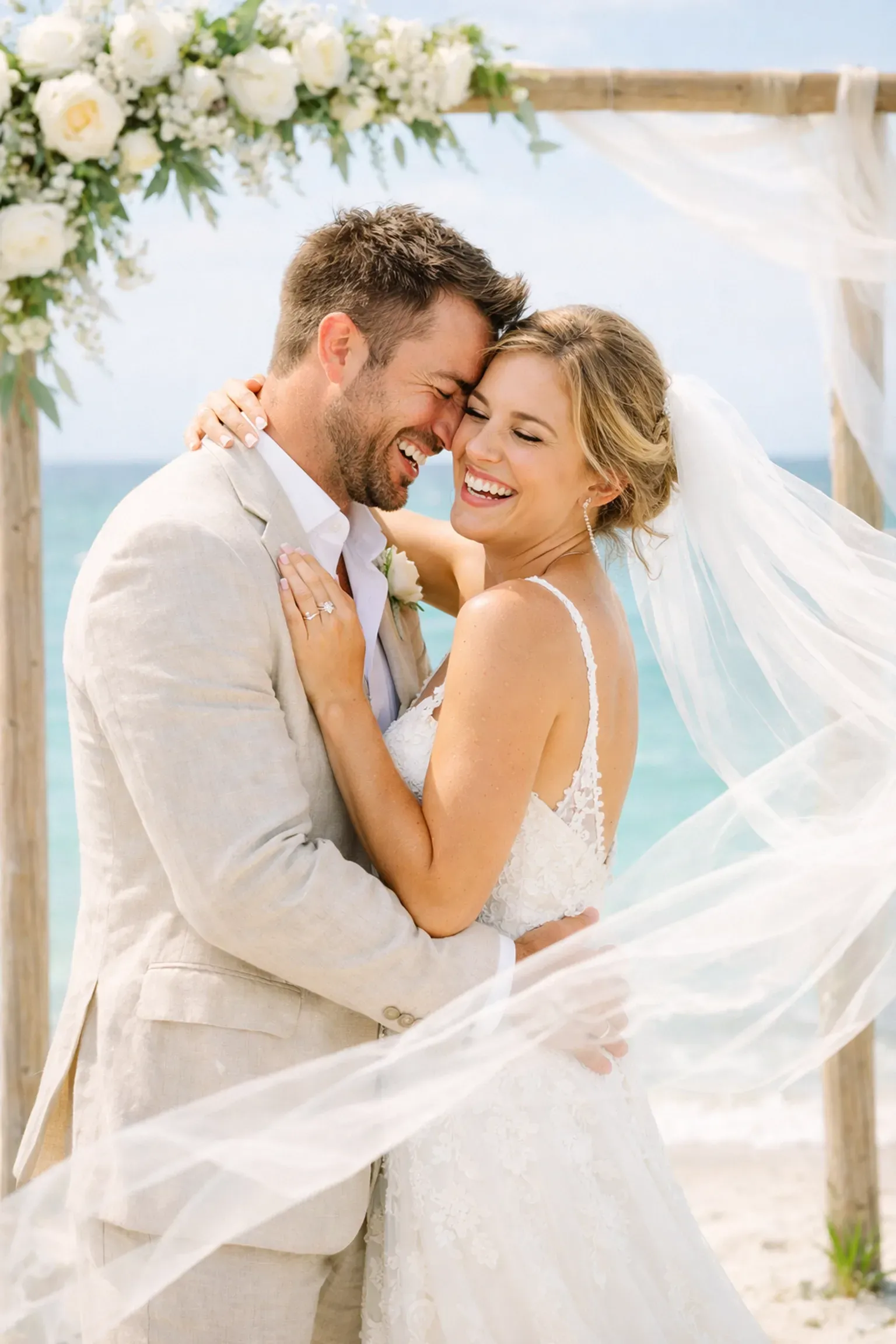 Happy couple embracing under a floral arch during their sunny Naples Florida beach wedding ceremony