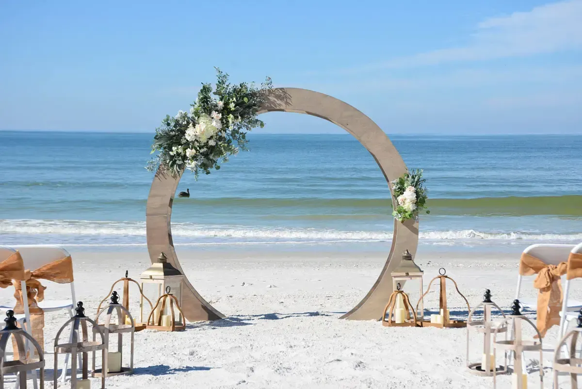 Wedding arch decorated with flowers on a beach, ocean in the background.