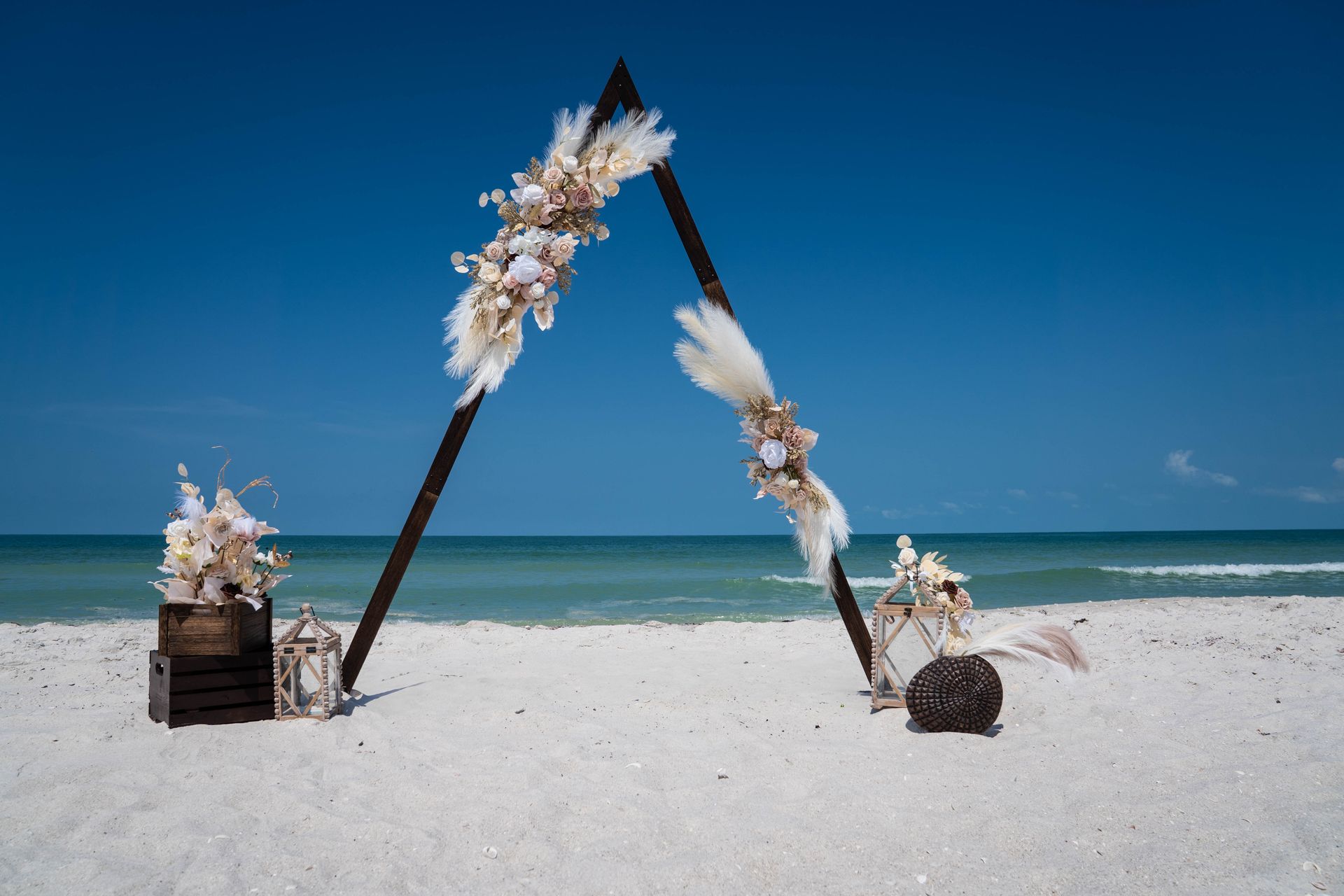 Beach wedding arch with floral decorations on a white sandy beach, against a blue sky.