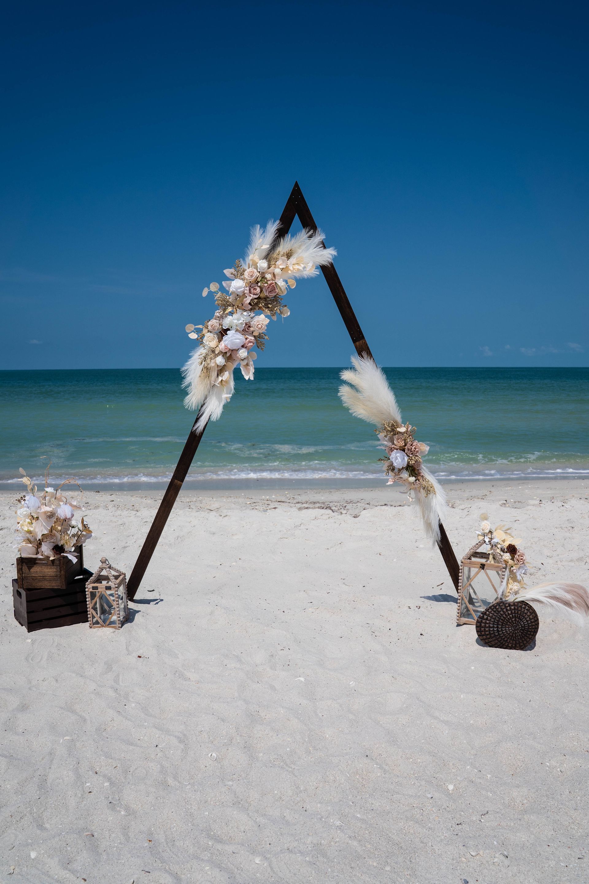 Beach wedding arch decorated with flowers against the ocean and blue sky.
