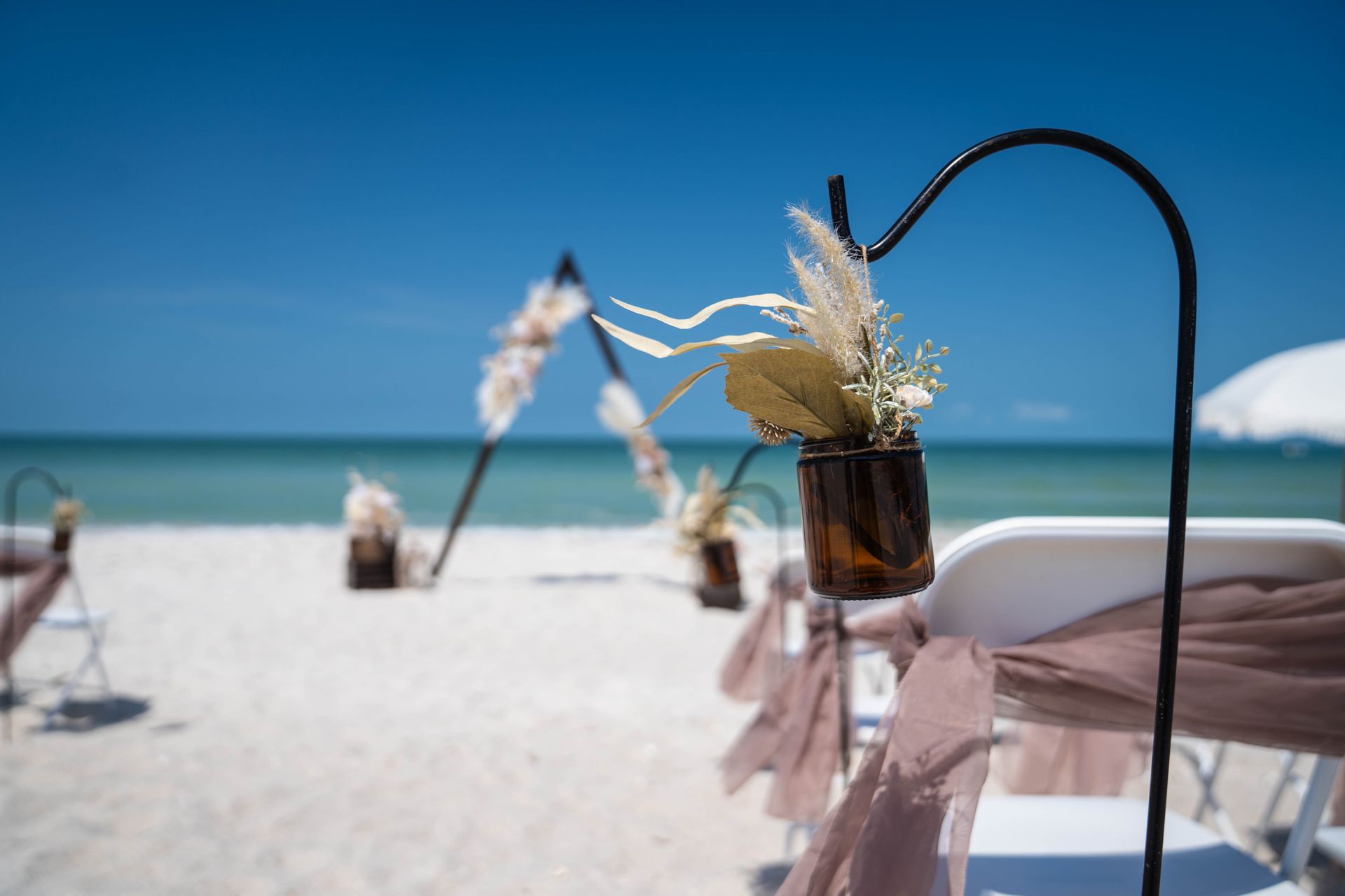 Beach wedding decorations with flowers in vases, white sand, and blue sky.