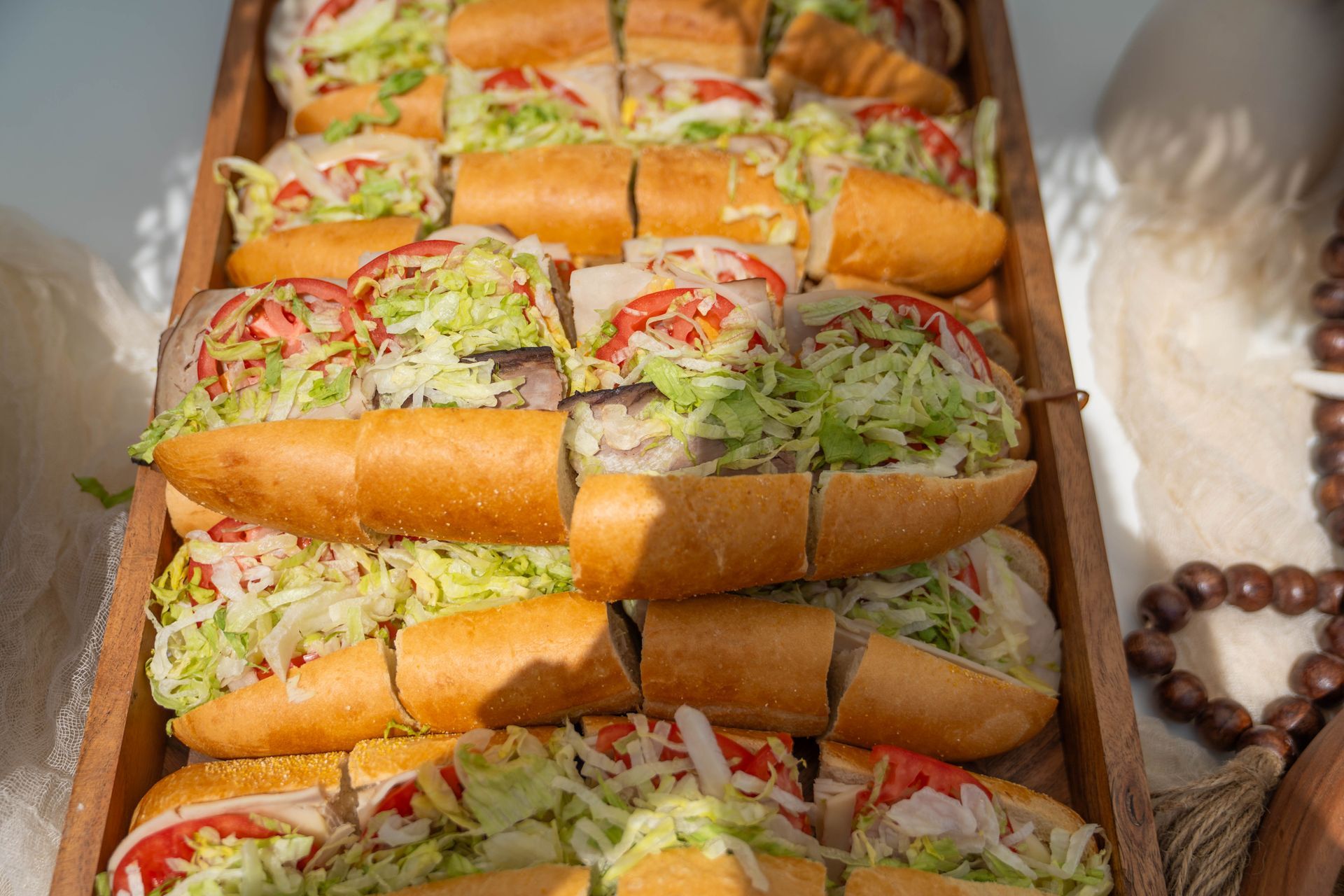 Sub sandwiches cut into halves, arranged on a wooden tray, with lettuce, tomato, and onion.