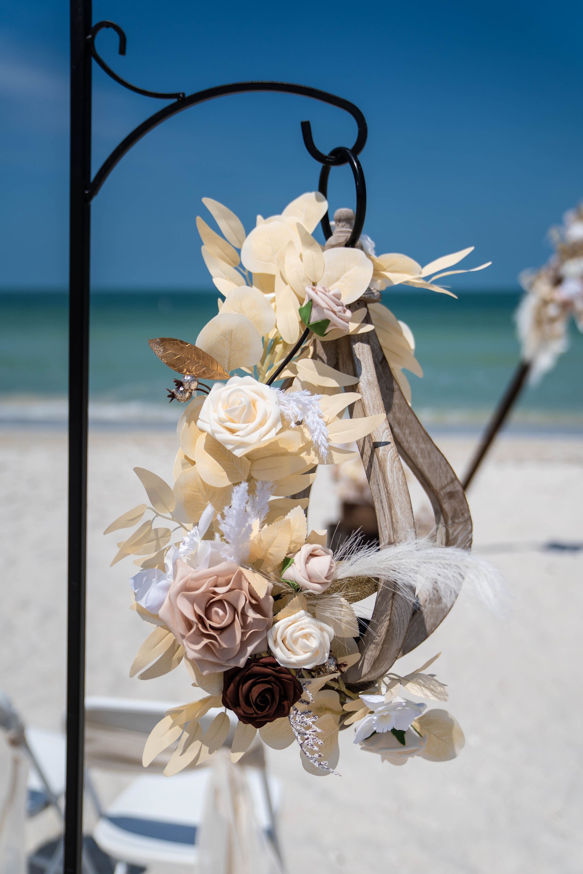 Floral decoration hanging on a black metal stand at a beach wedding, with ocean in the background.