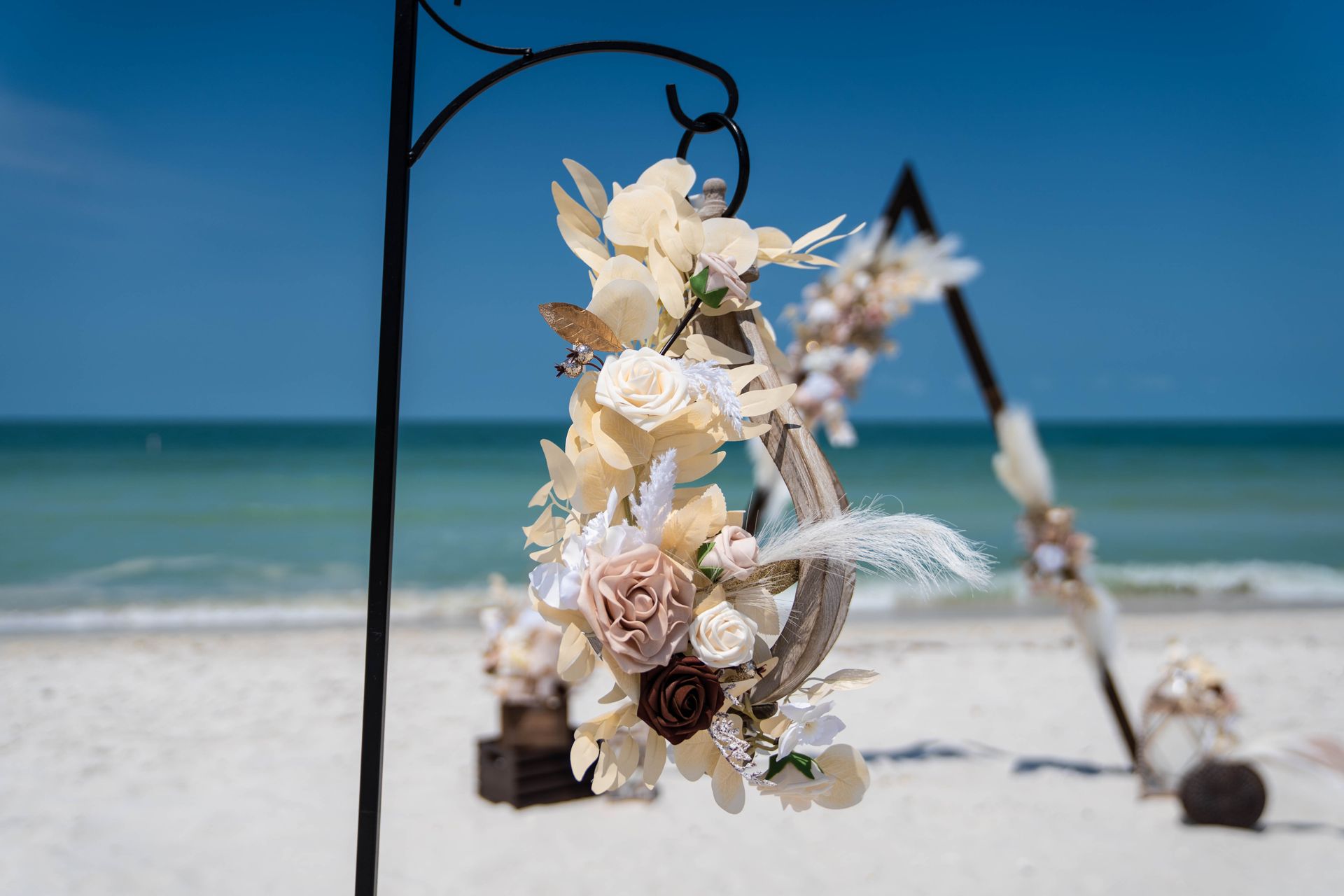 Beach wedding decor with floral wreath, triangle arch, and ocean background.