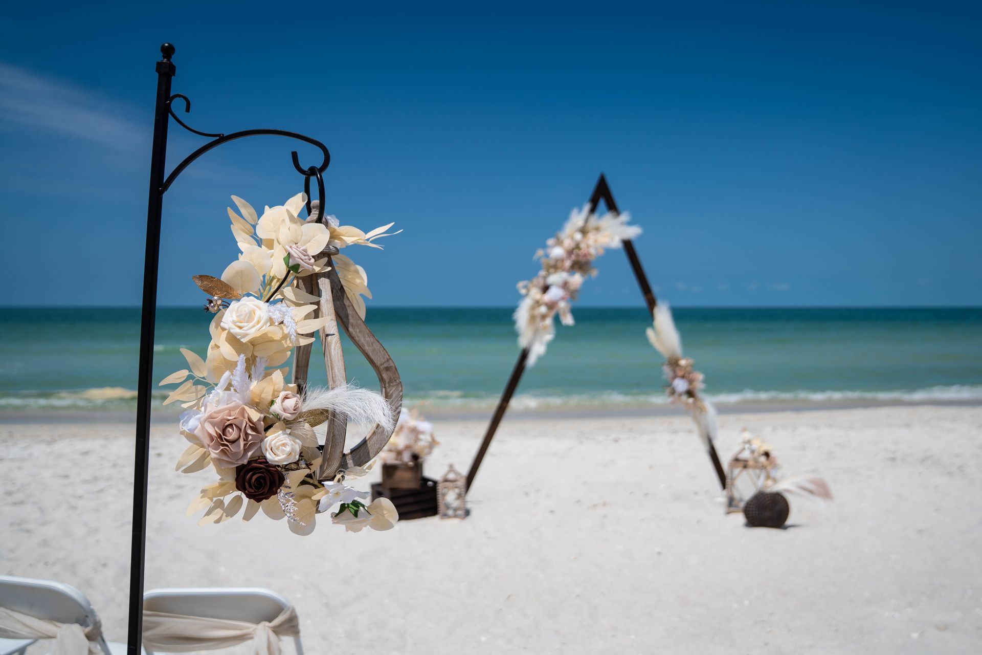 Beach wedding setup with floral decorations, against a backdrop of the ocean and blue sky.