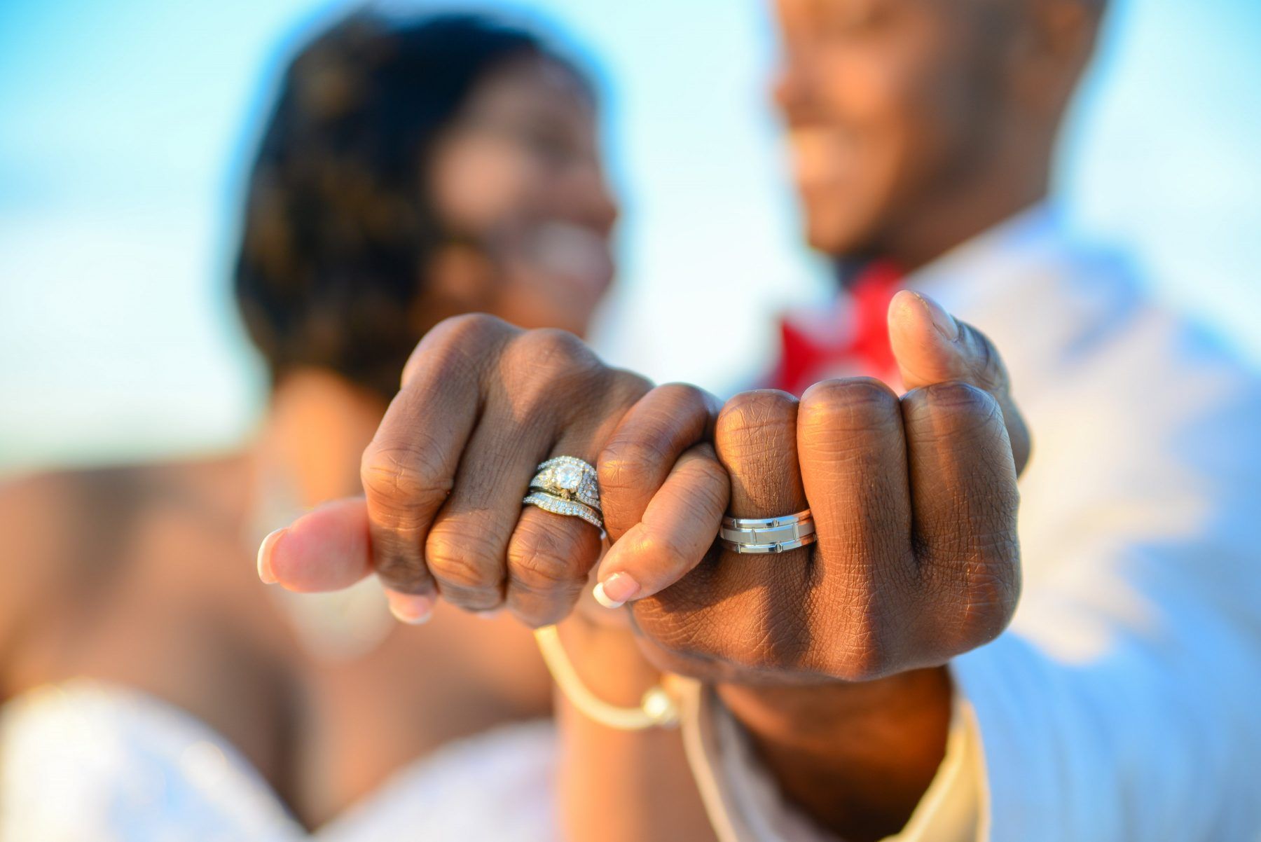 Couple holding hands, showing wedding rings, with ocean in background.