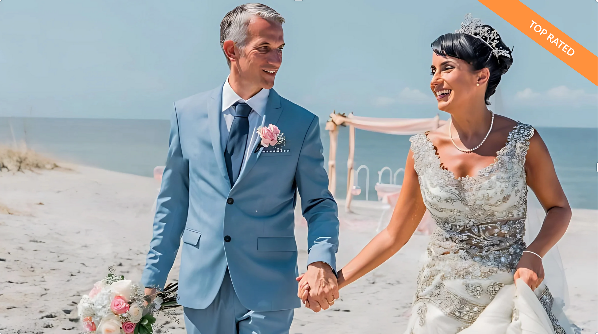 Bride and groom holding hands, smiling, walking on beach. Groom in blue suit, bride in white dress.