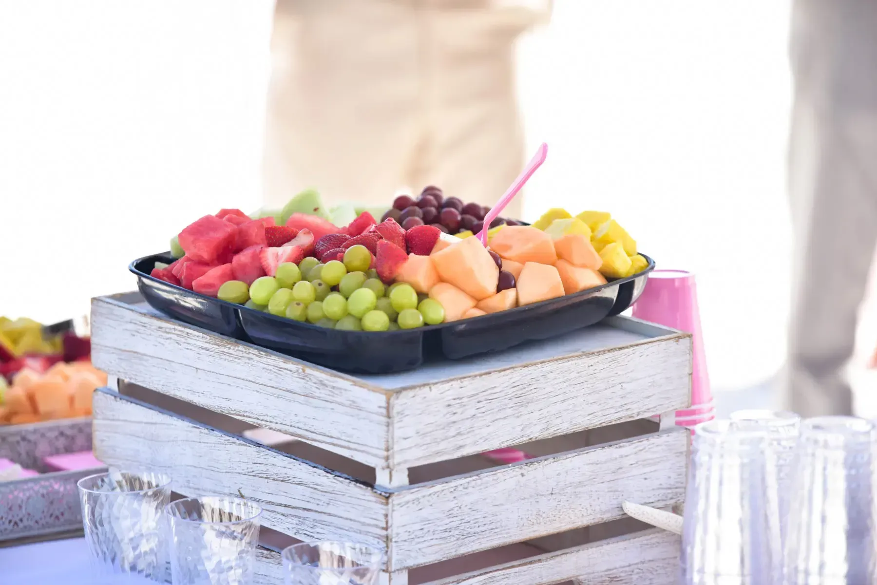 Fruit platter on a white wooden crate. Includes watermelon, grapes, cantaloupe, strawberries, and mango.