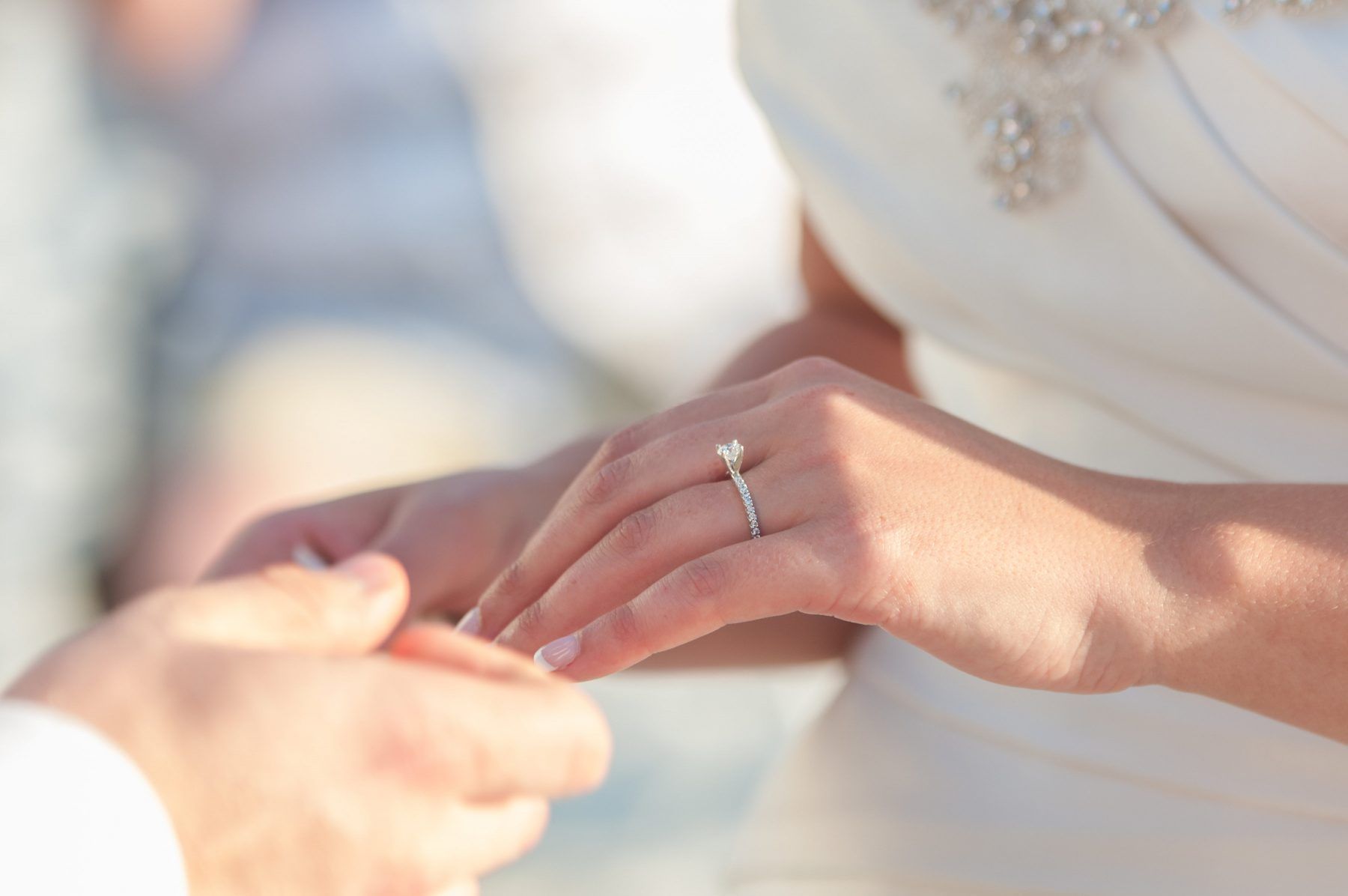 A bride wearing a white dress and engagement ring, has her hand held by another person during a wedding ceremony.