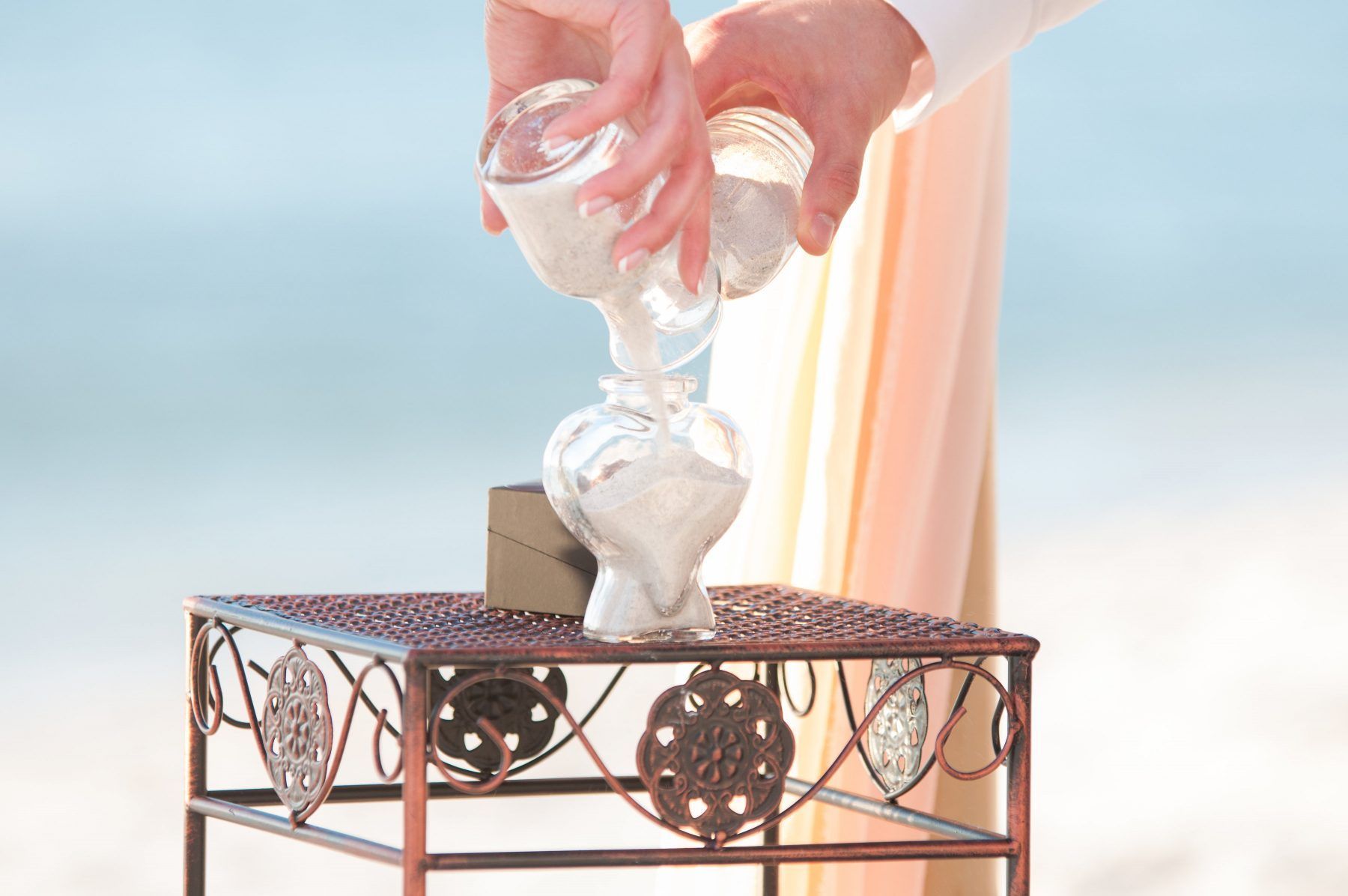 Couple pouring sand into a glass vase during a beach wedding ceremony.