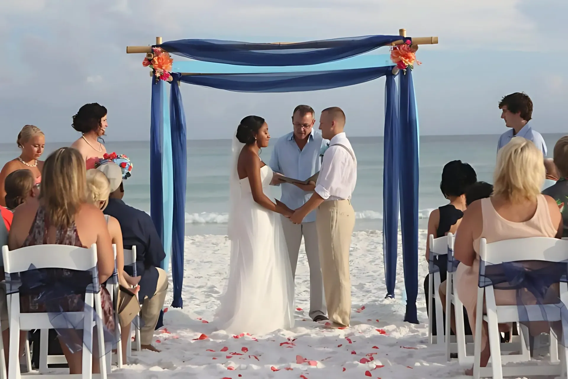 Couple exchanging vows at beach wedding under draped arch.