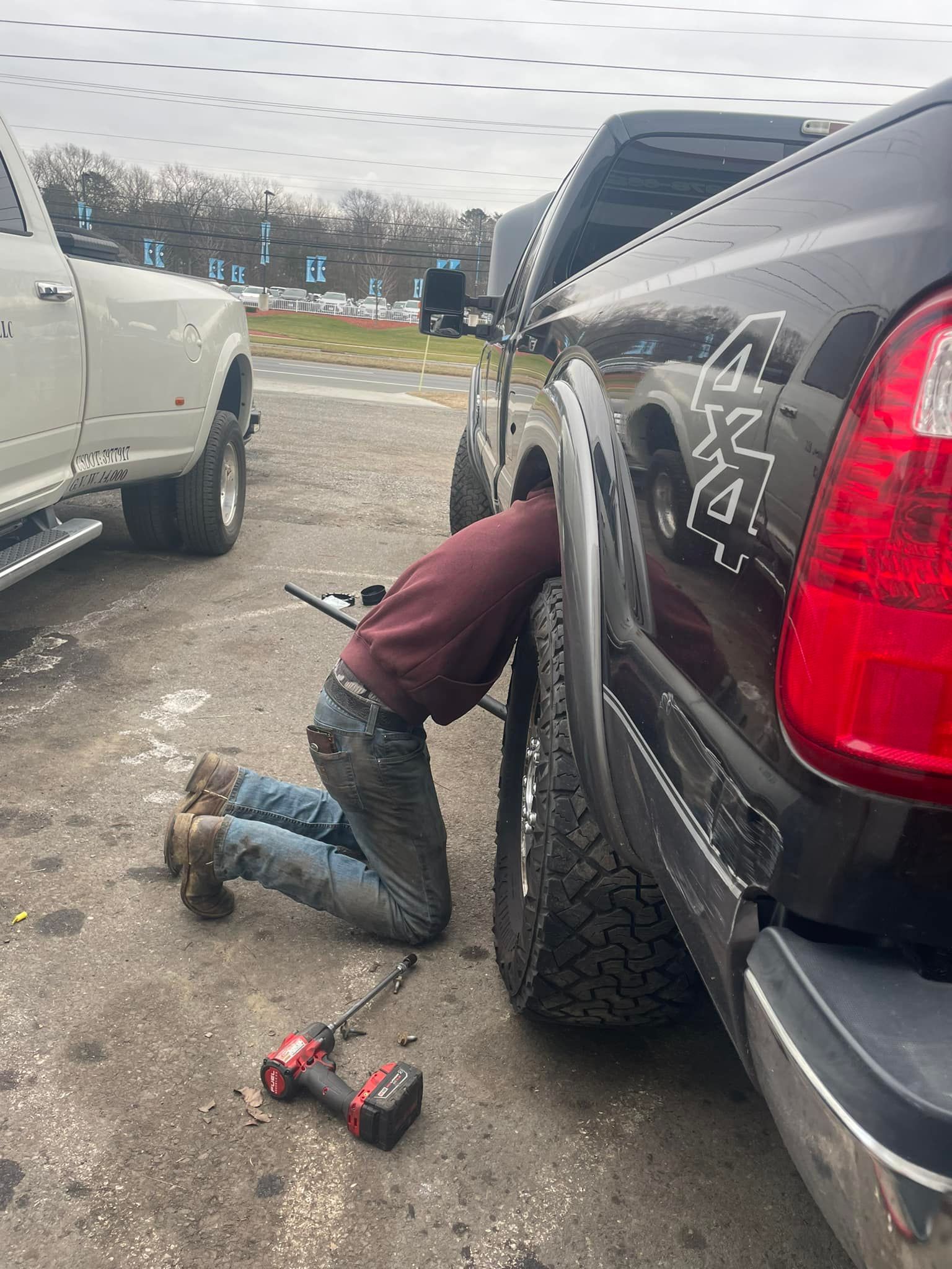 A man is kneeling down next to a truck in a parking lot.