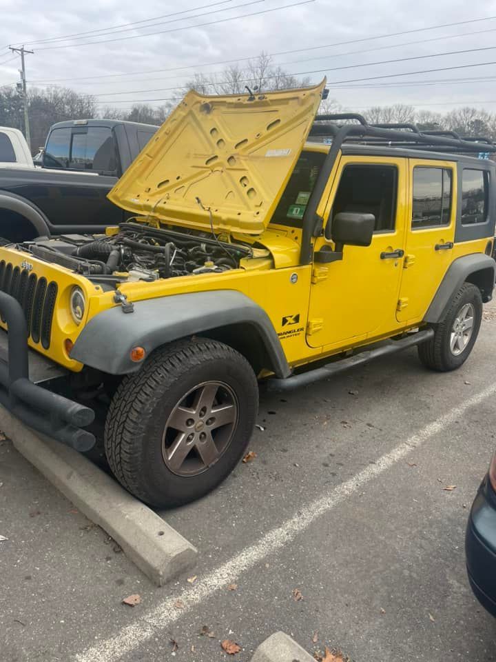 A yellow jeep with the hood up is parked in a parking lot.