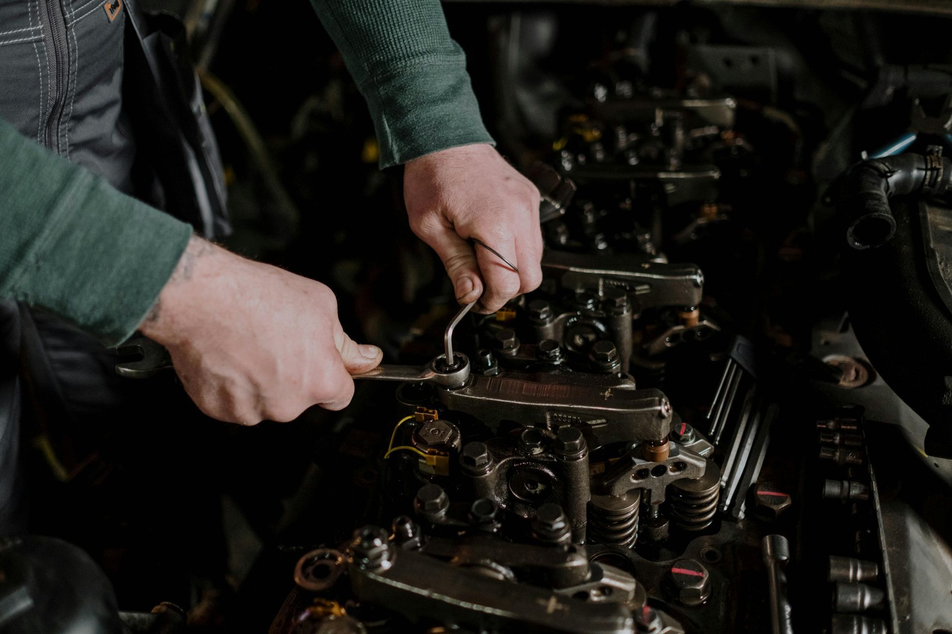 Mechanic's hands using a wrench on an engine, dark setting.