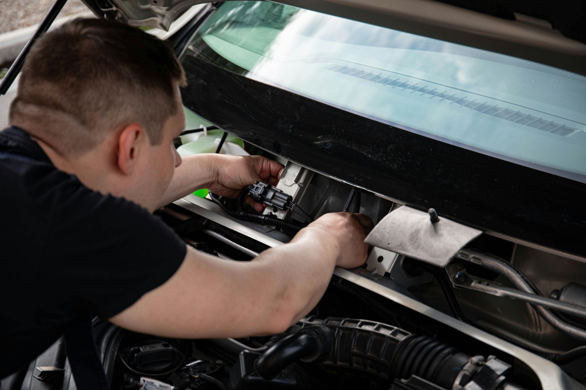 Mechanic working under a car’s hood in a garage, using tools on the engine