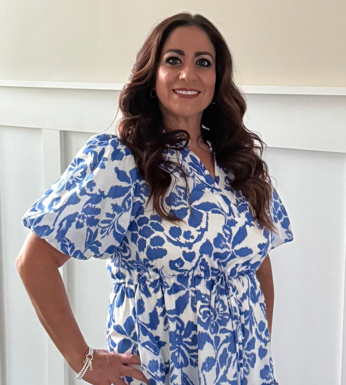 A woman with long red hair is standing in front of a tree and looking at the camera.