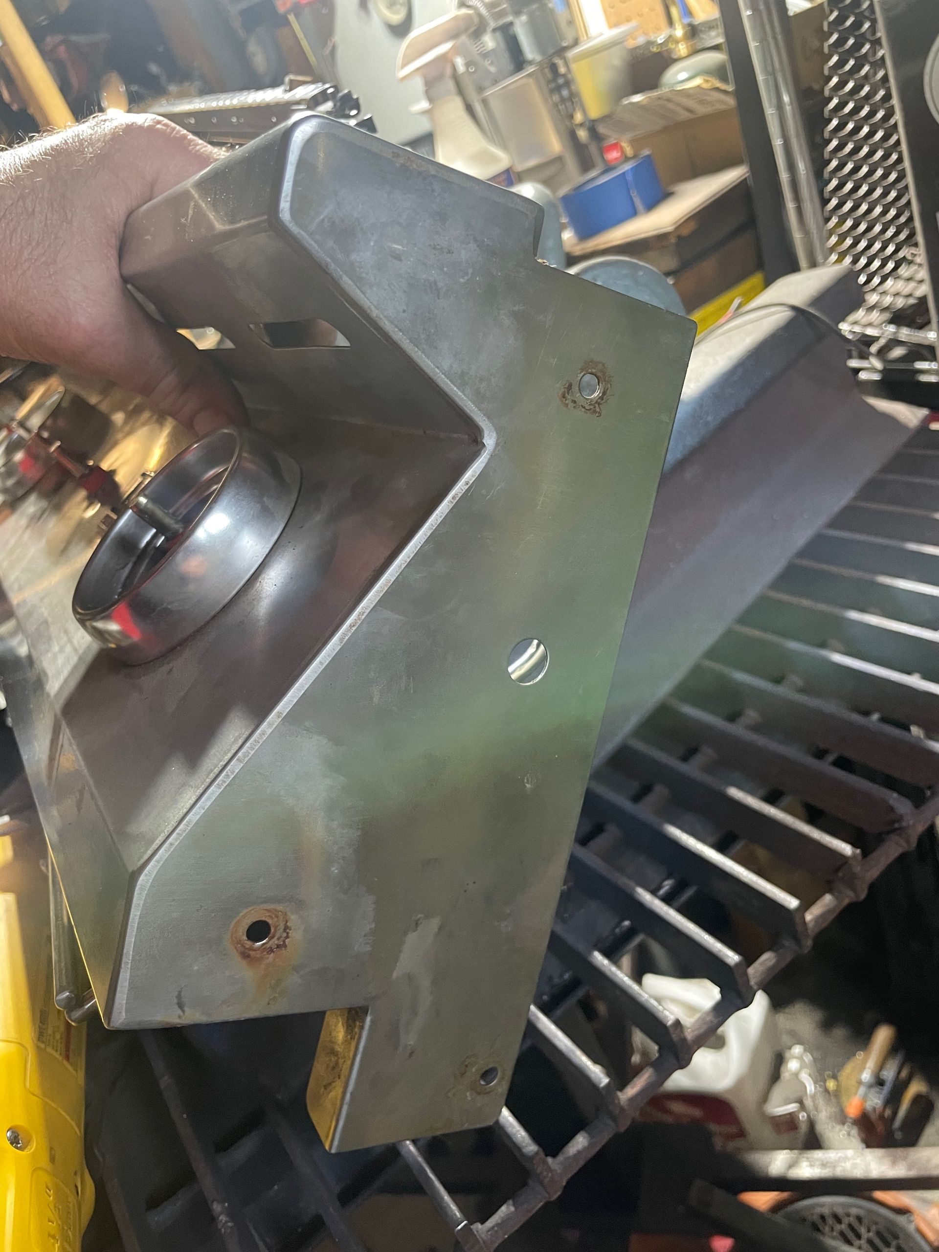 A hand holding a silver metal barbecue part with a circular vent, over a grill.