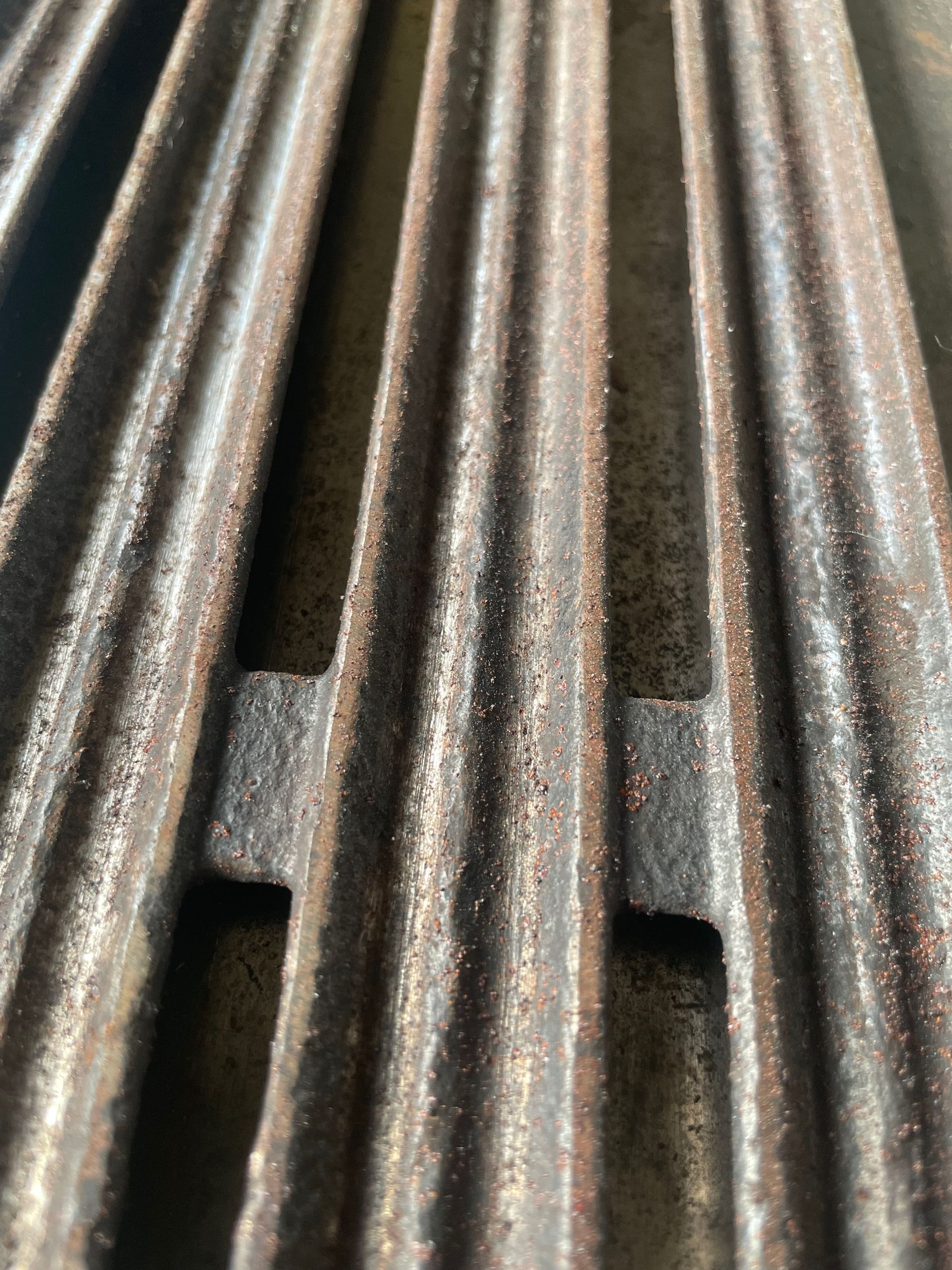 Close-up of a rusty metal grill grate with raised ridges and support pieces.