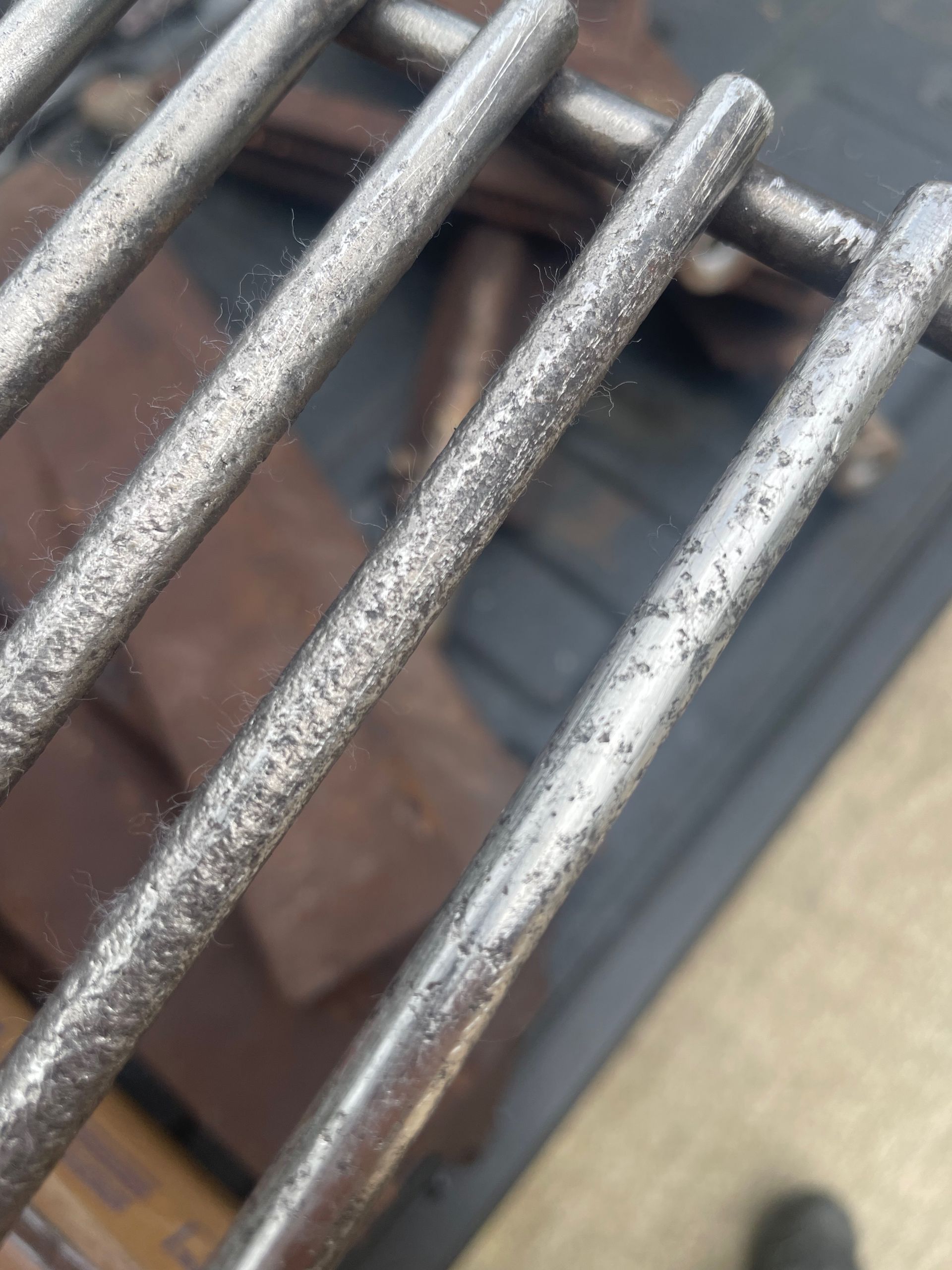 Close-up of a rusted metal grill grate with a blurry background of reddish-brown bricks.