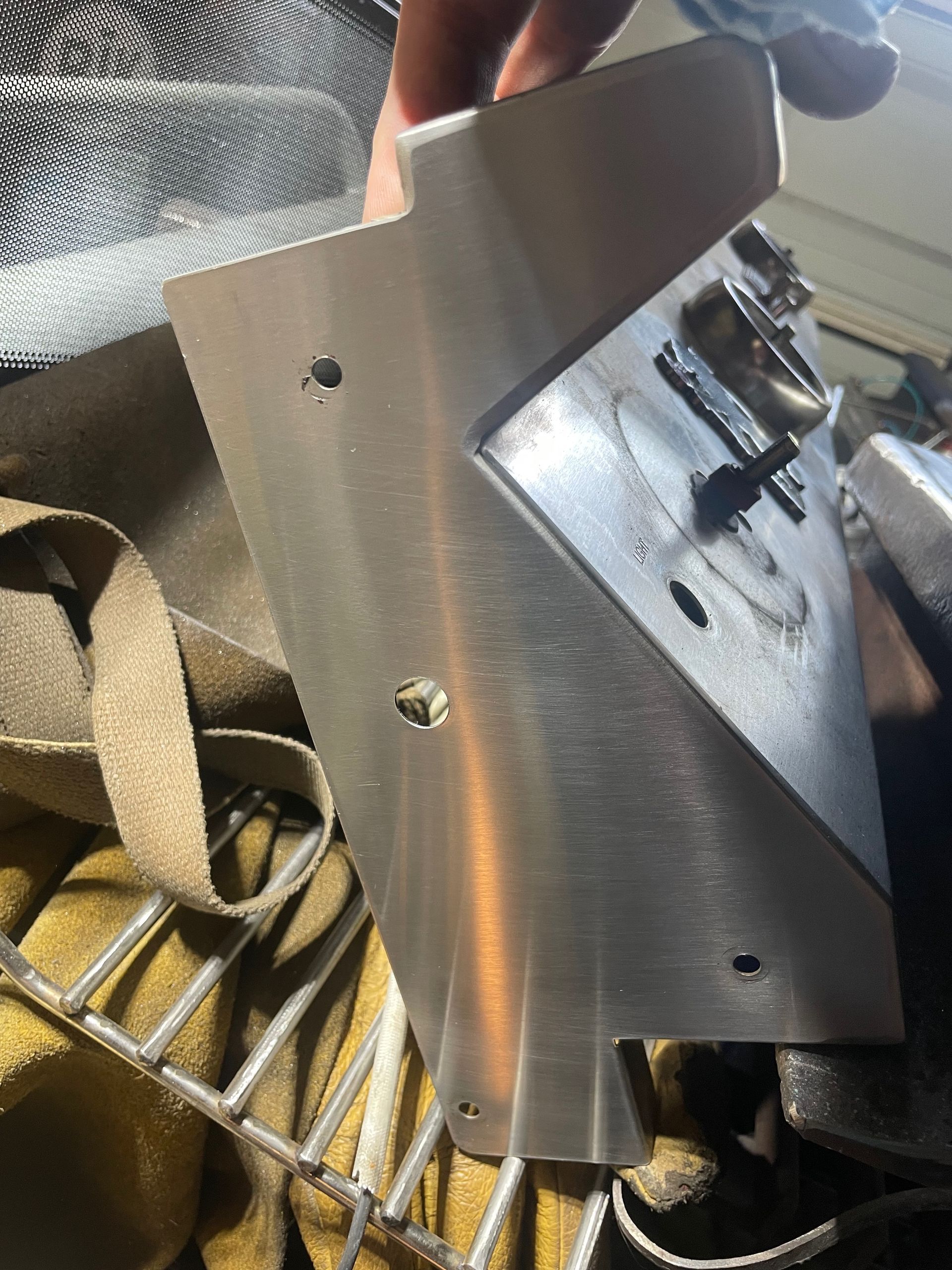 A person holding a metallic part with several holes, near a vise and welding equipment.