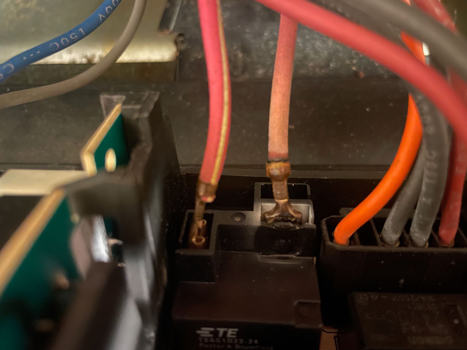 Close-up of electrical wiring. Two red wires are attached to a black component, one with a slightly burnt appearance.