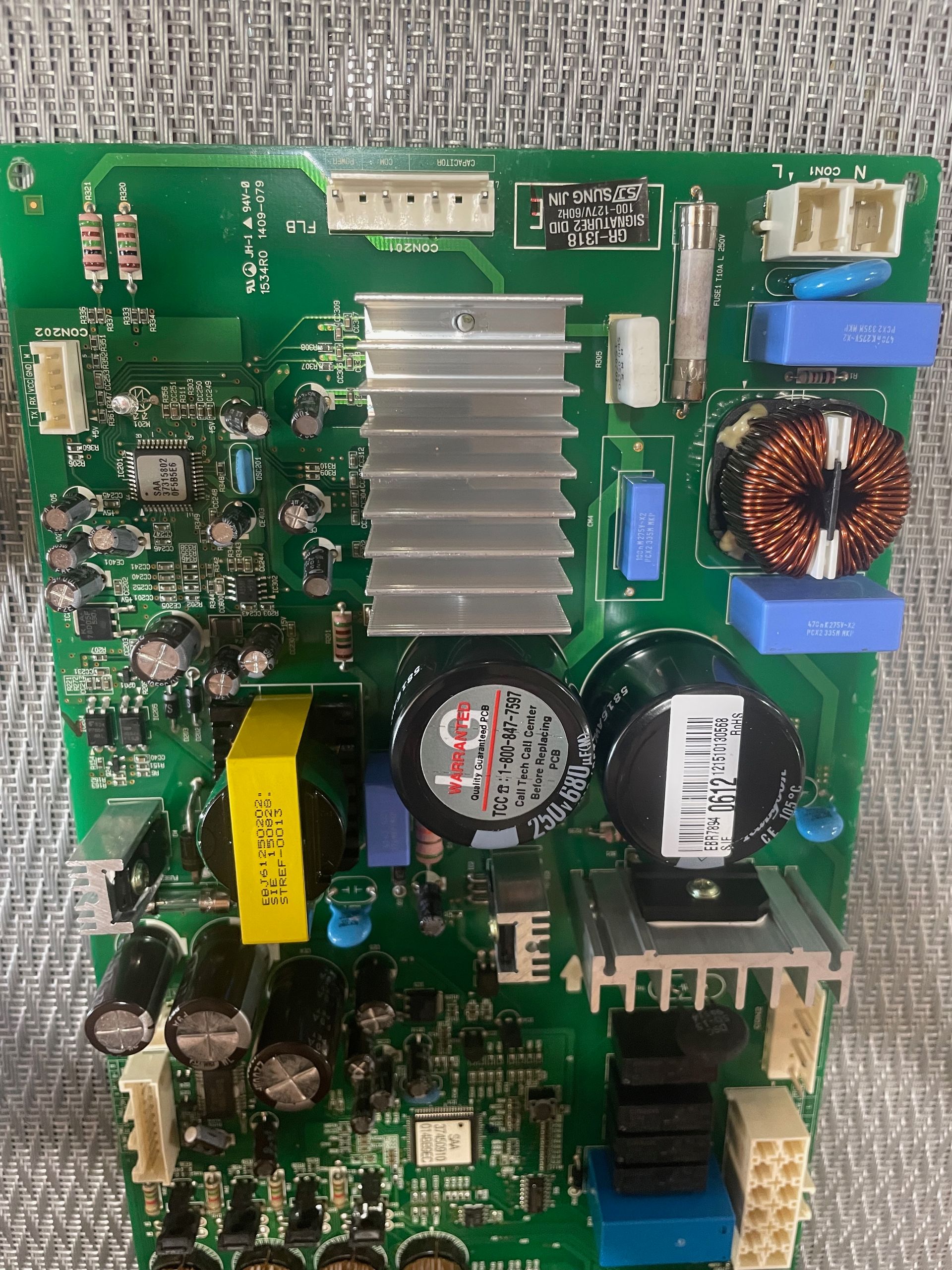Green circuit board with various electronic components, including a heat sink, capacitors, and coils.