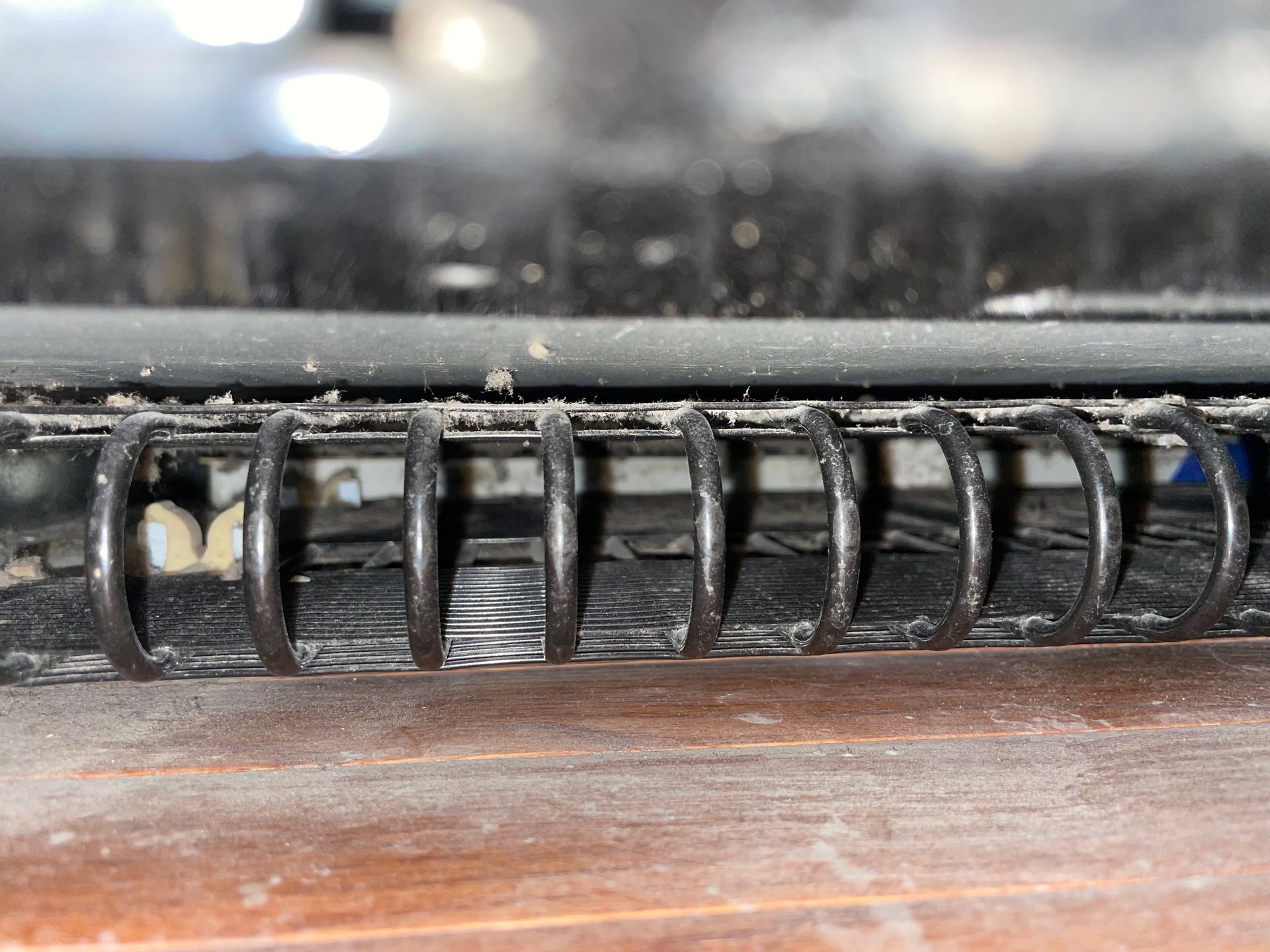 Close-up of a black spiral notebook spine with a wood surface beneath, covered in dust and debris.