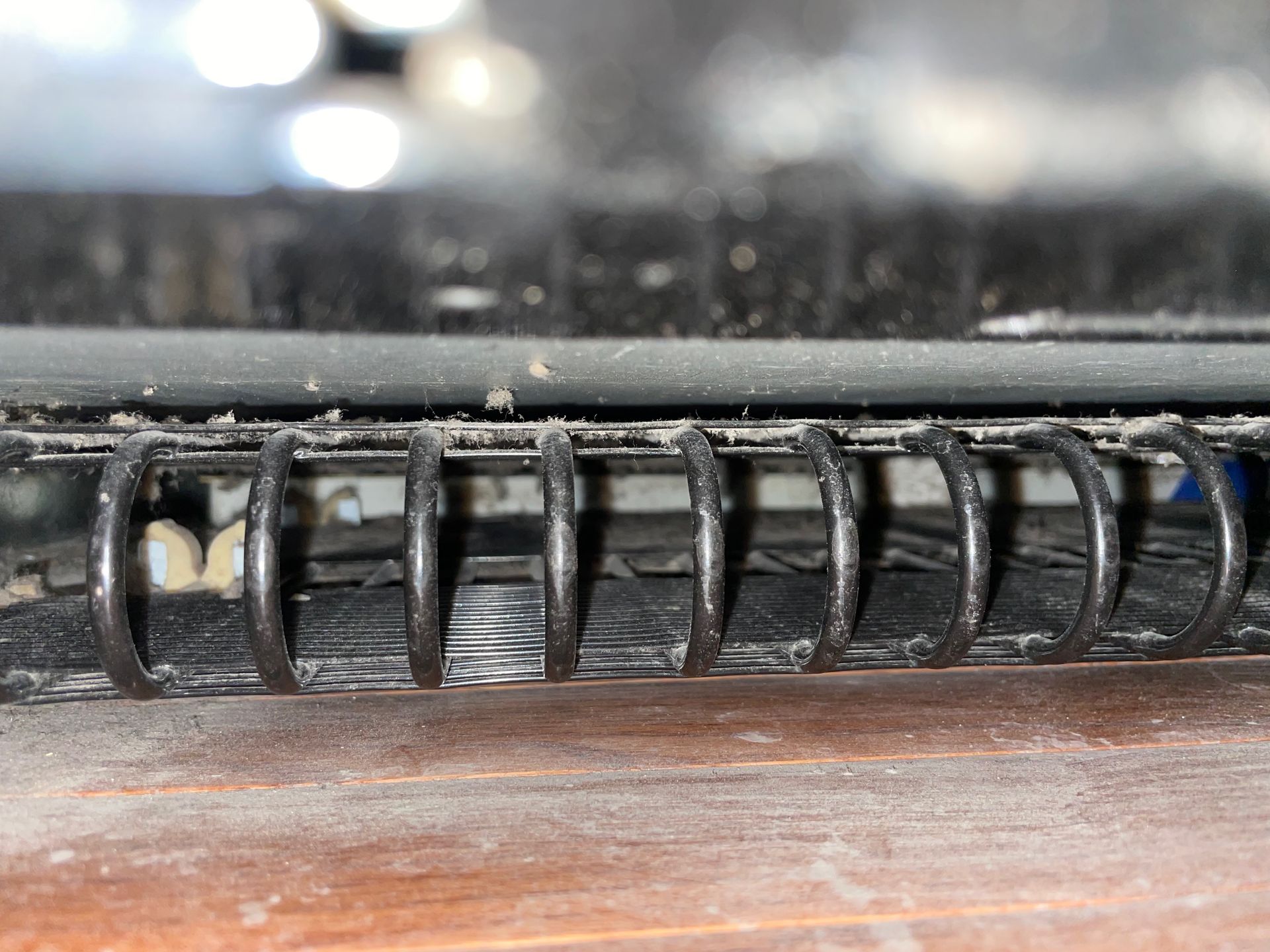Close-up of a black spiral binding on a notebook, resting on a dusty wooden surface.