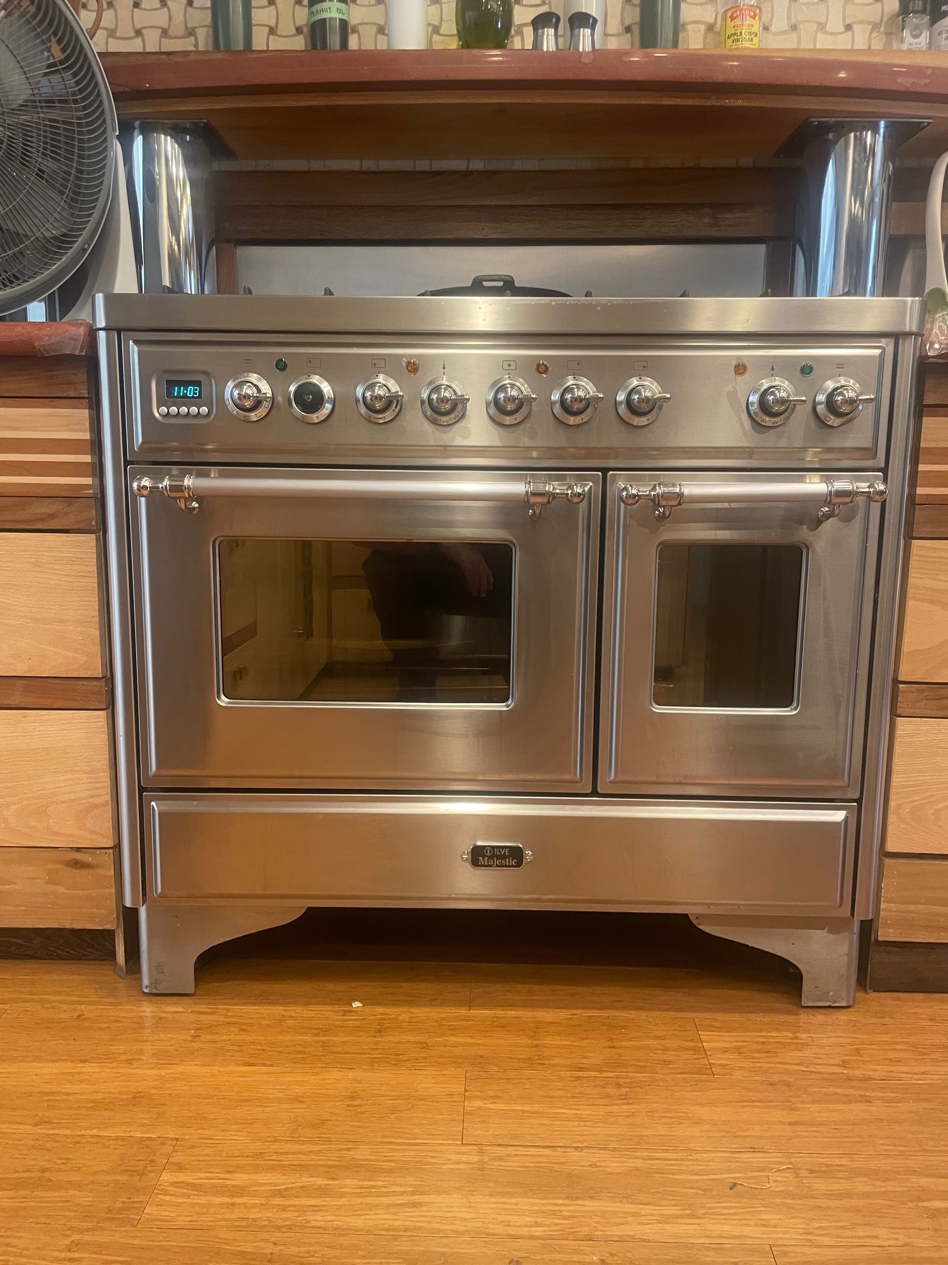 Stainless steel range oven with multiple burners and two oven doors, set in a wooden kitchen.