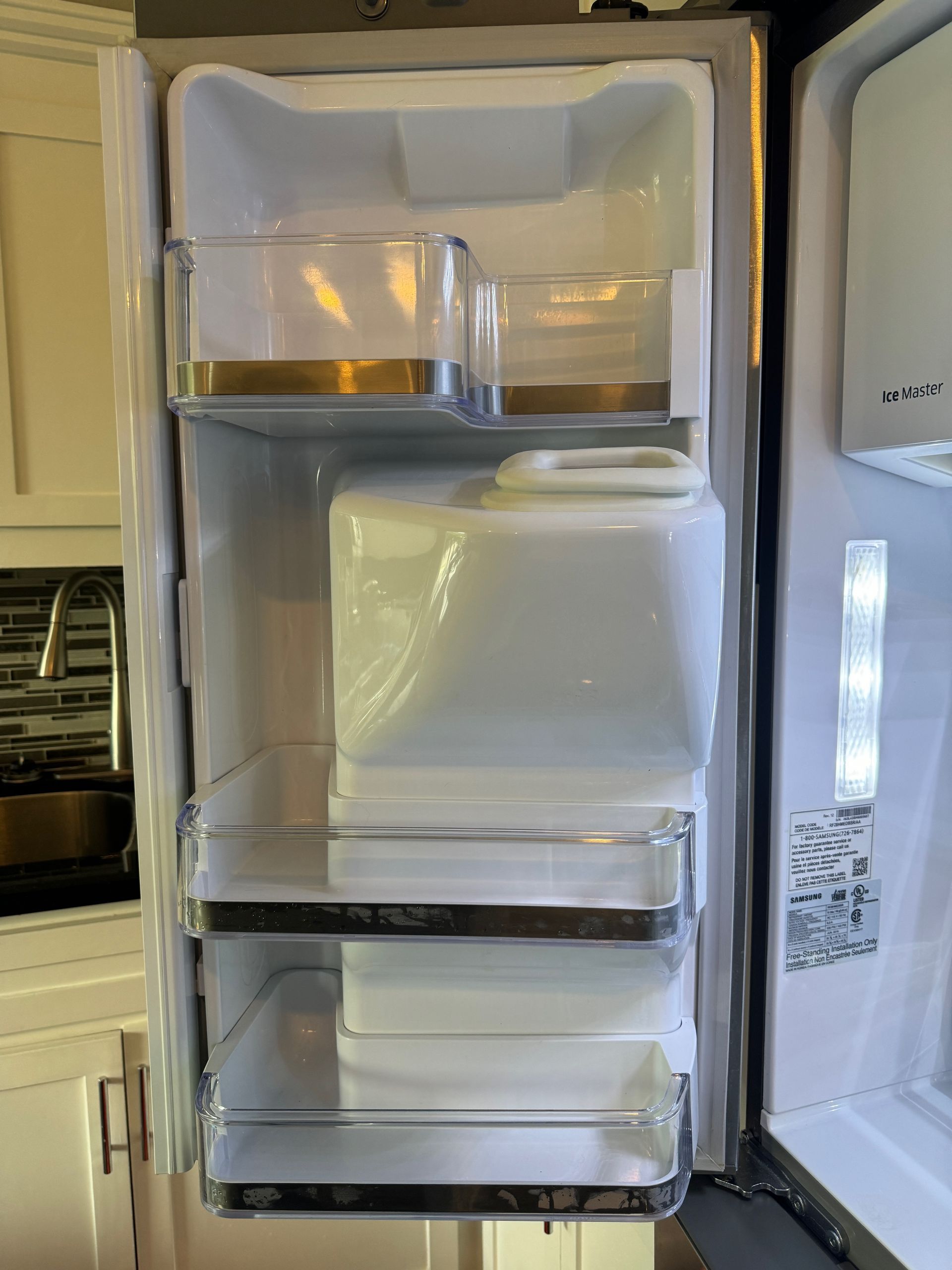 Empty refrigerator interior with clear bins and shelving. The door is open, revealing a white interior and bright lighting.