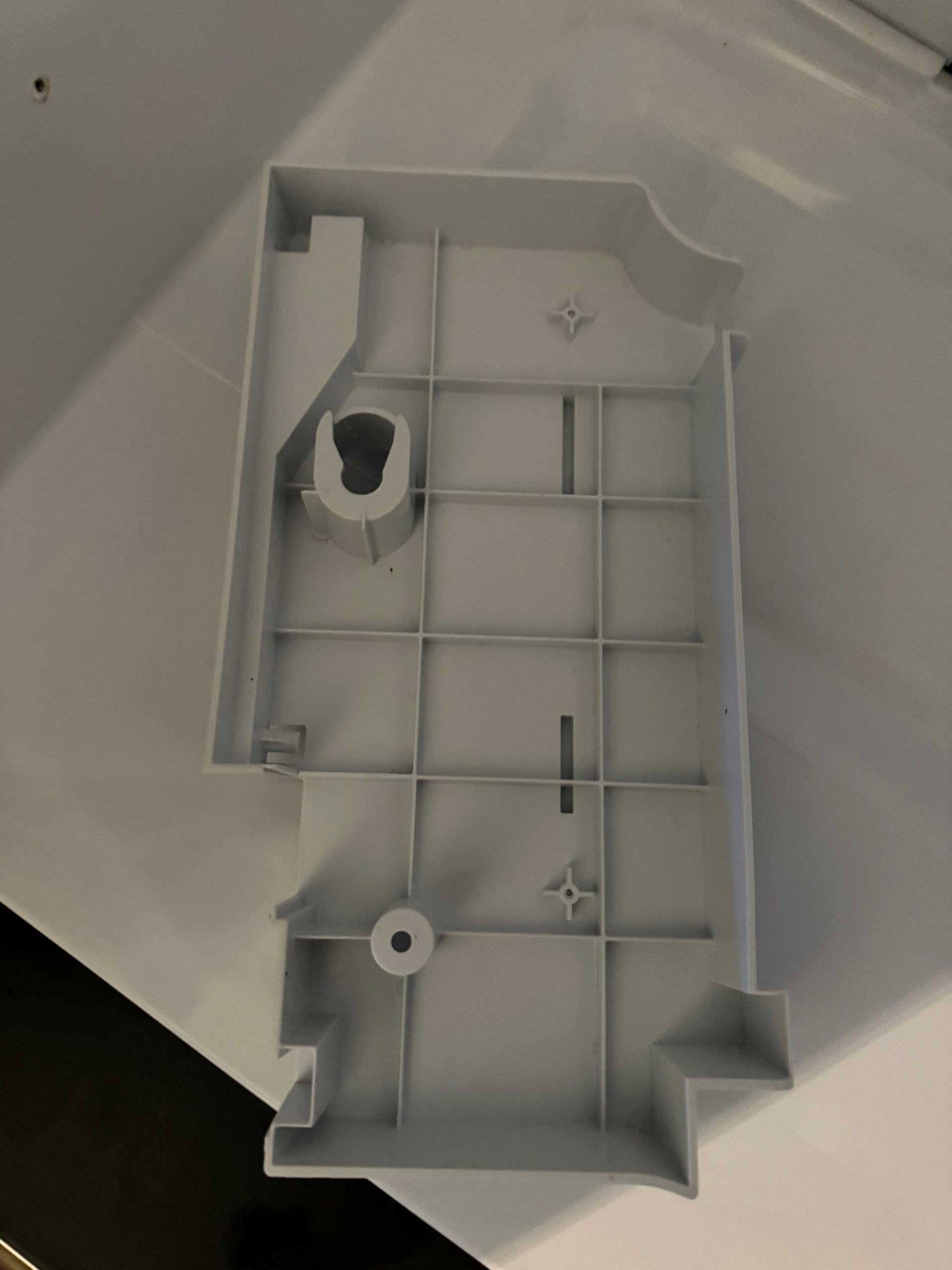 White plastic base with a grid pattern and various holes and protrusions, likely from an appliance.