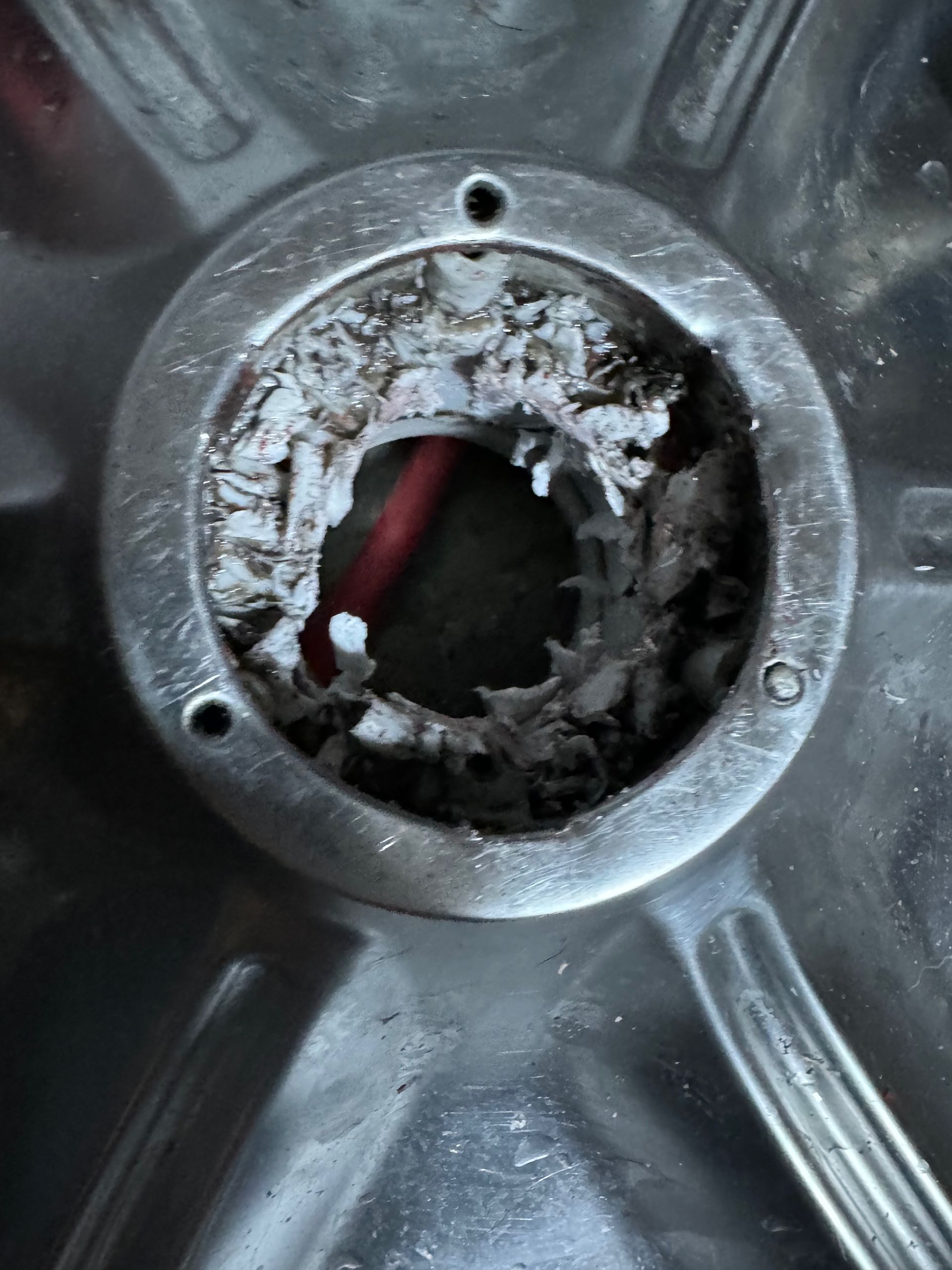Close-up of a metal wheel hub with significant buildup of white, crusty deposits around a central opening with visible wires.