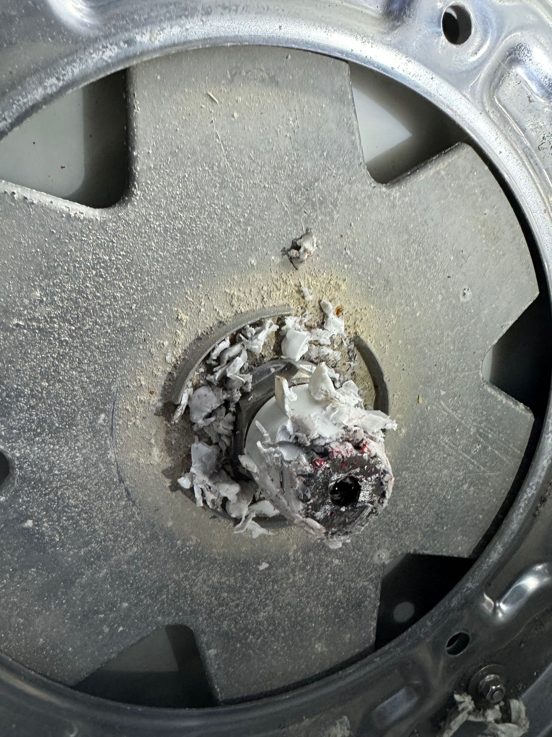 Close-up of a gray and white appliance part. A central hub is covered in charred material, surrounded by a circular metal frame.