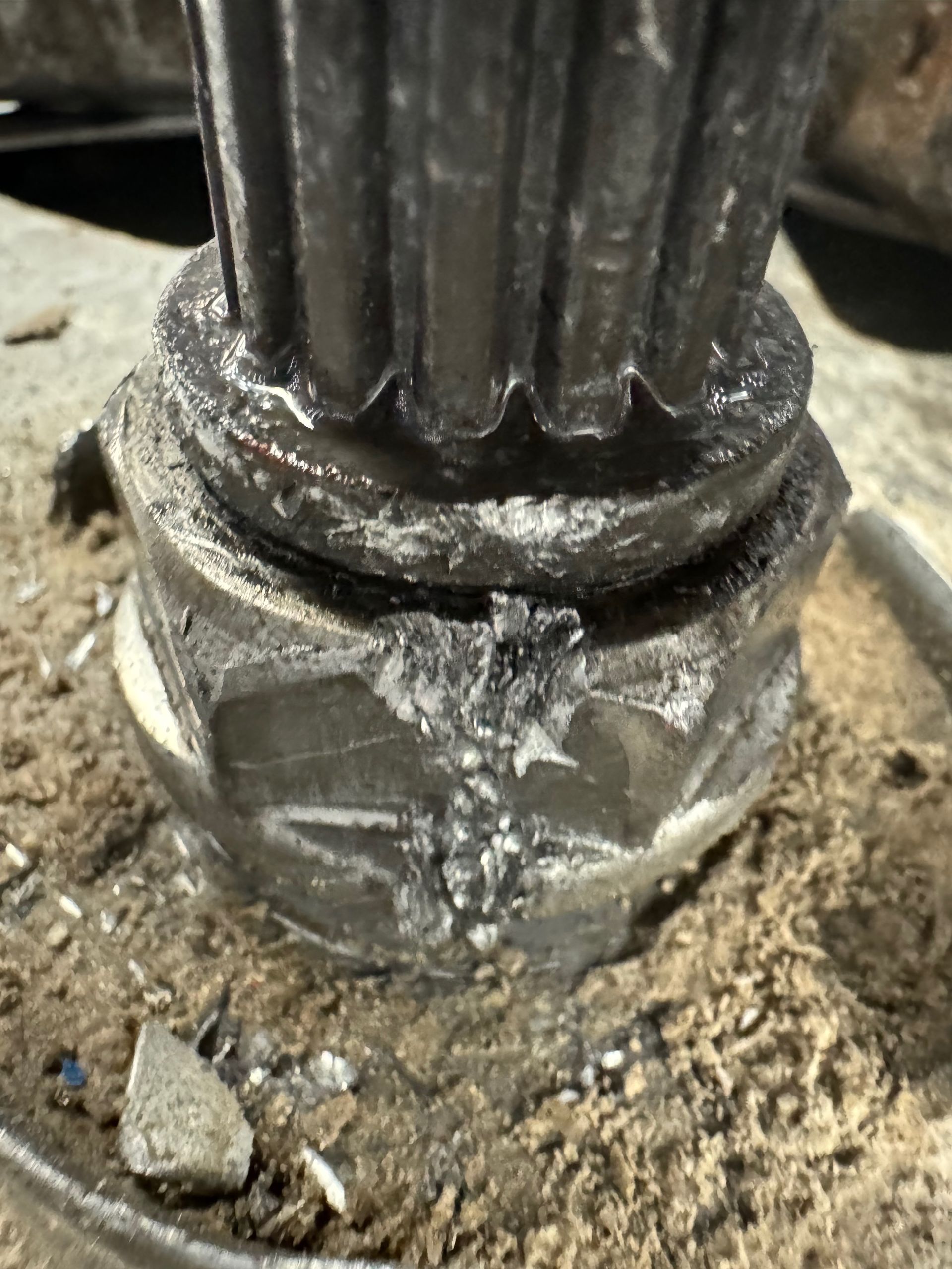 Close-up of a damaged, black gear shaft with a crushed base, covered in debris.