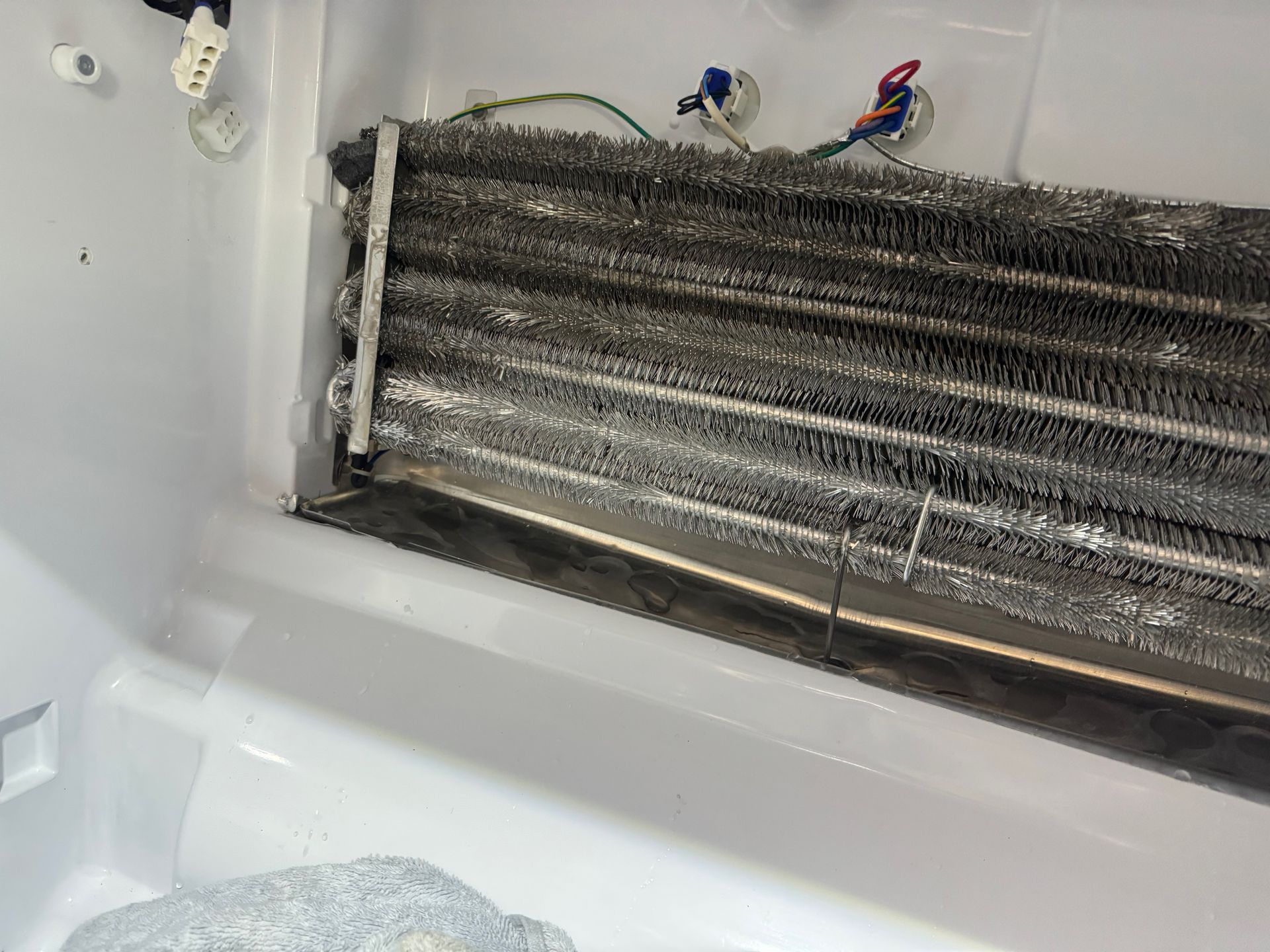 Interior of a refrigerator freezer compartment with a heavily frosted evaporator coil, covered in ice crystals.