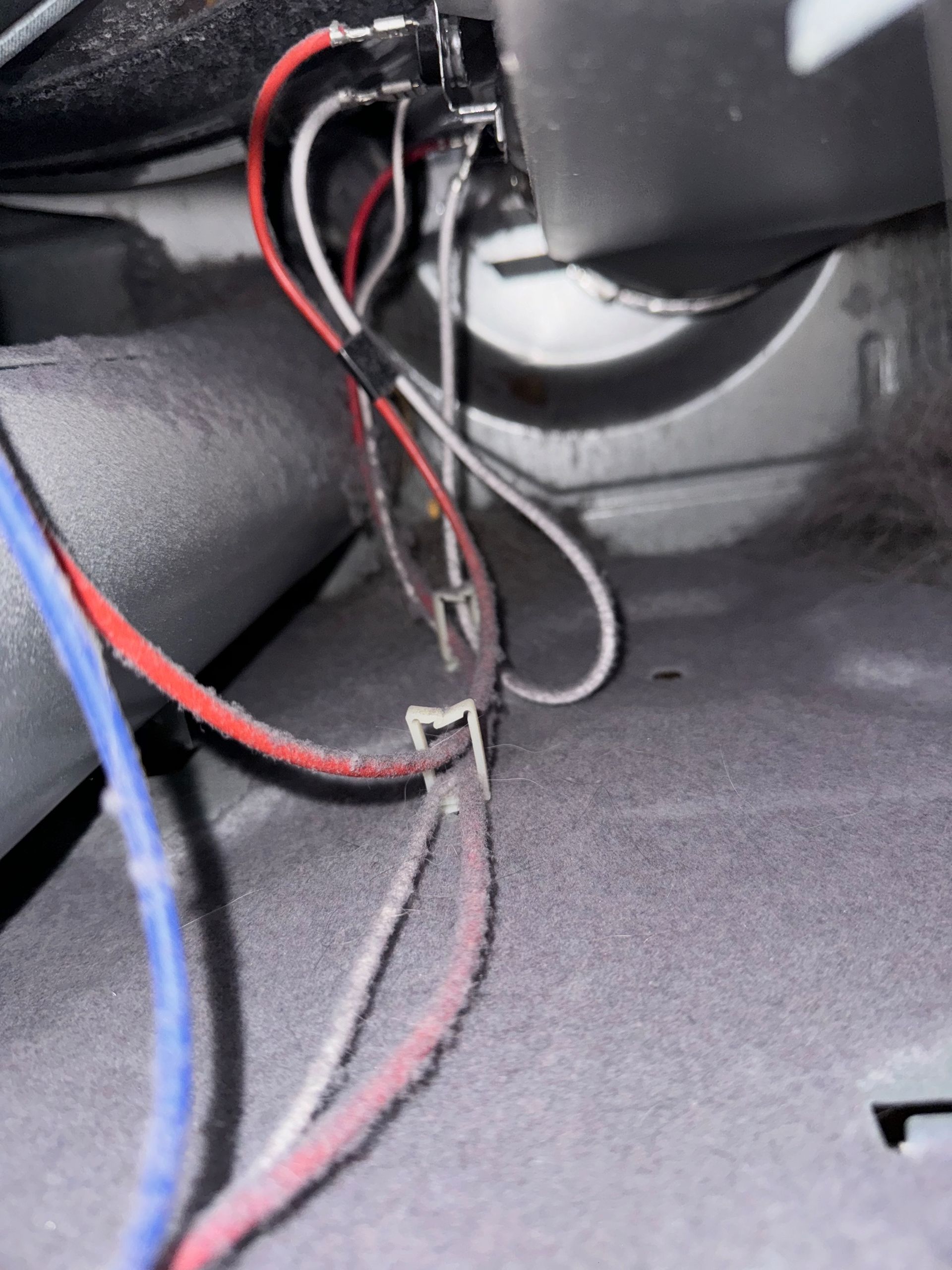 Close-up of tangled electrical wires, mostly red, white, and blue, inside a gray compartment.