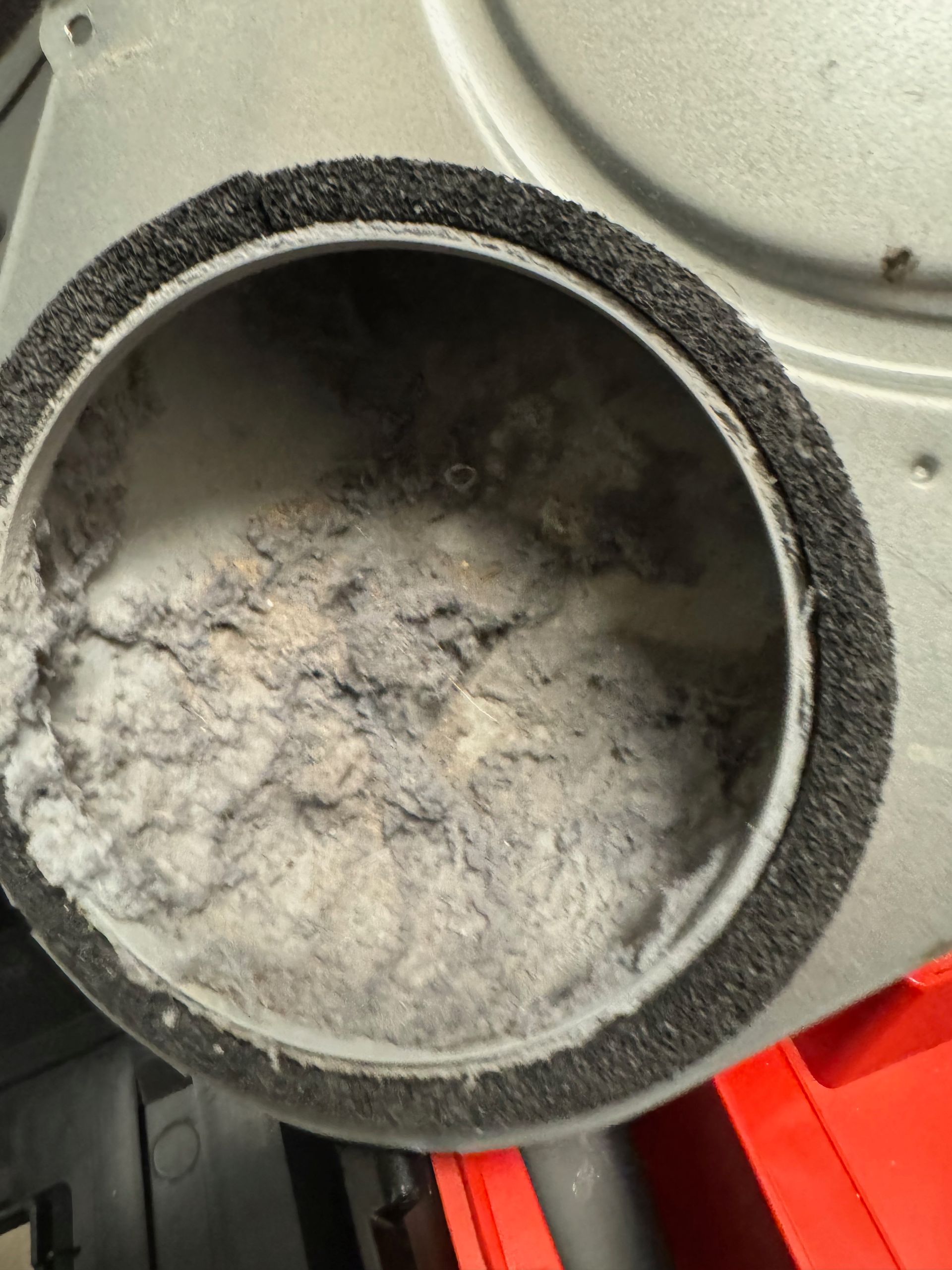 A close-up view of a dryer lint trap filled with a thick, grey mass of lint. The round opening has a black, padded rim.