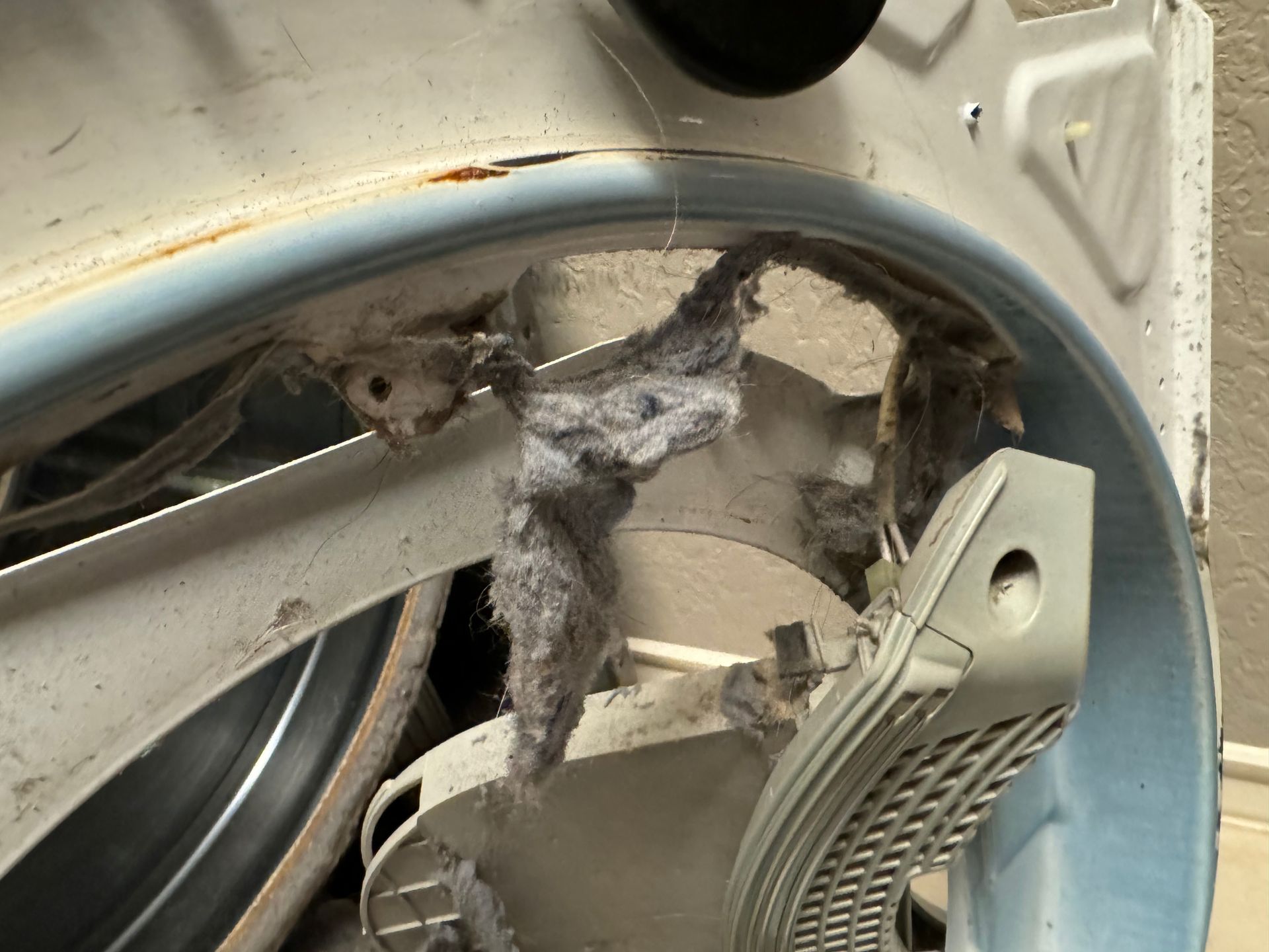 Close-up of a dryer's lint trap area clogged with grey lint. The dryer's interior metal frame is visible.
