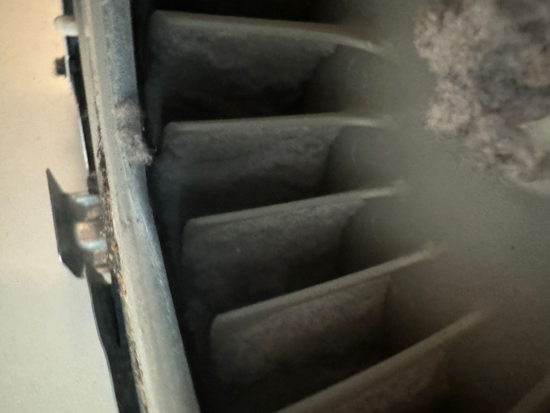 Close-up of a dusty air vent. The vent's slats are coated in a thick layer of gray dust and debris.