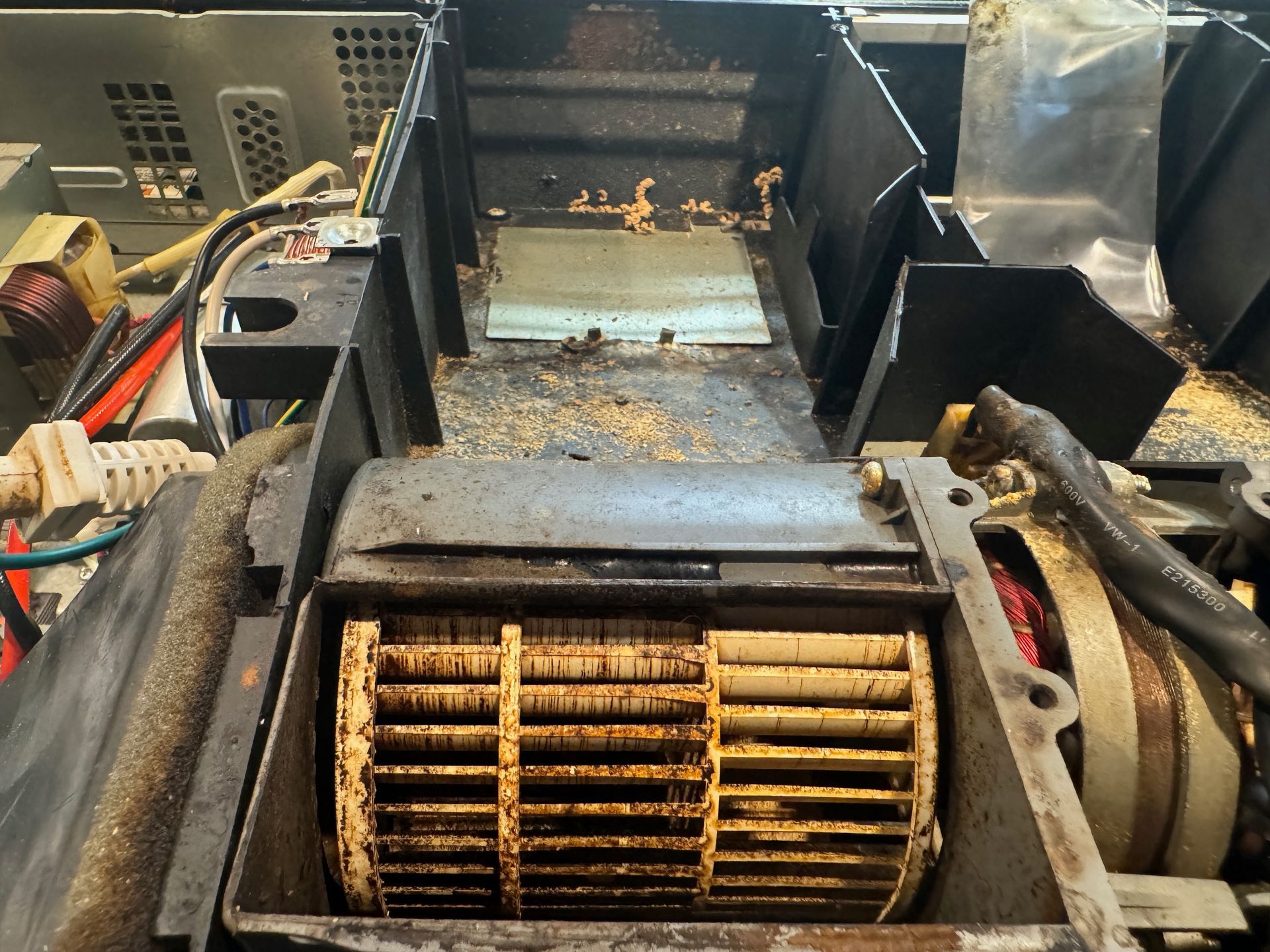 Close-up of a dirty, disassembled air conditioner unit with a fan and electrical components visible.