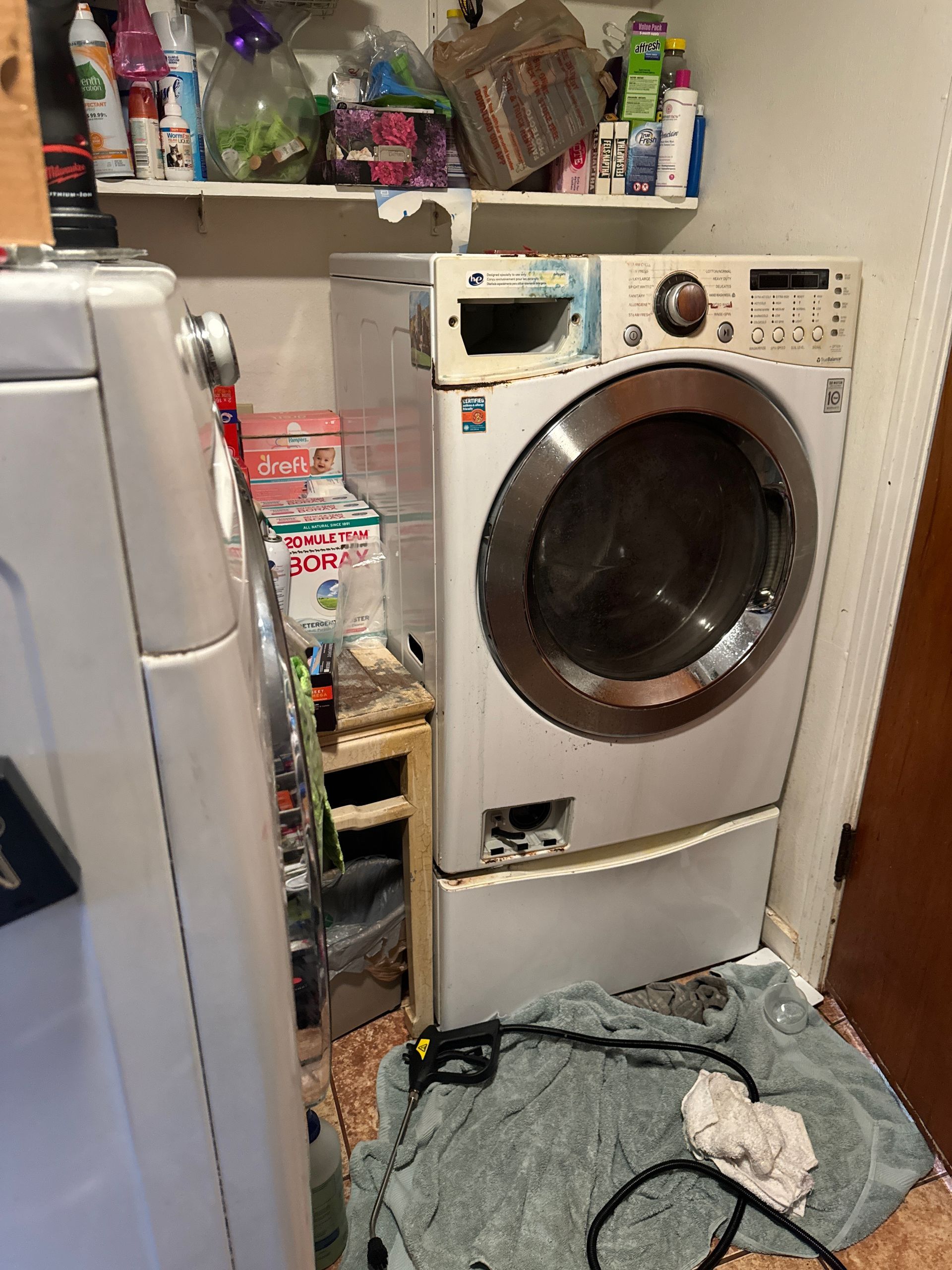 A front-loading washing machine in a cluttered laundry area.  It's light grey with a partially opened door and visible wiring.