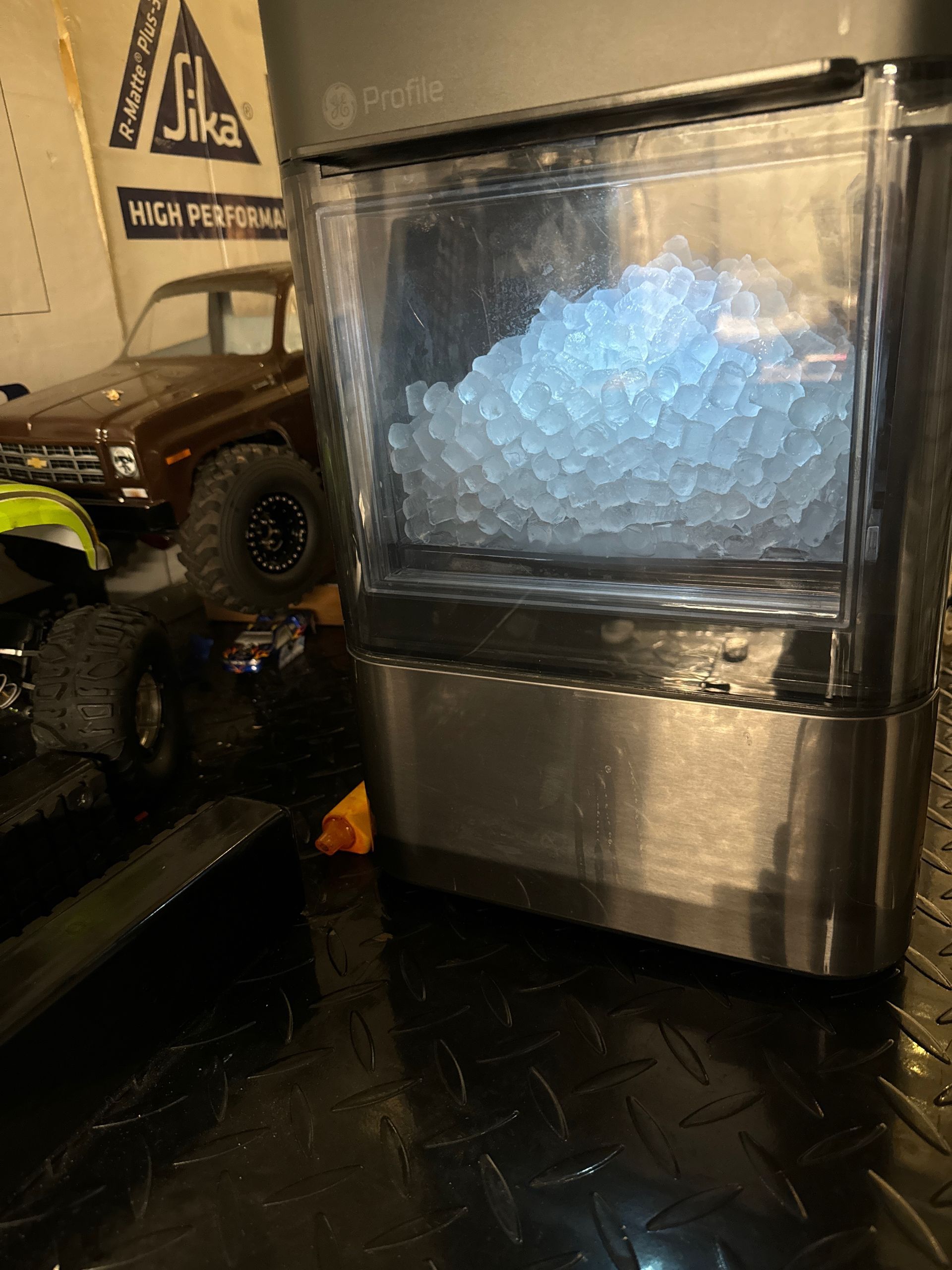 A stainless steel countertop ice maker filled with nugget ice, in front of a toy truck.