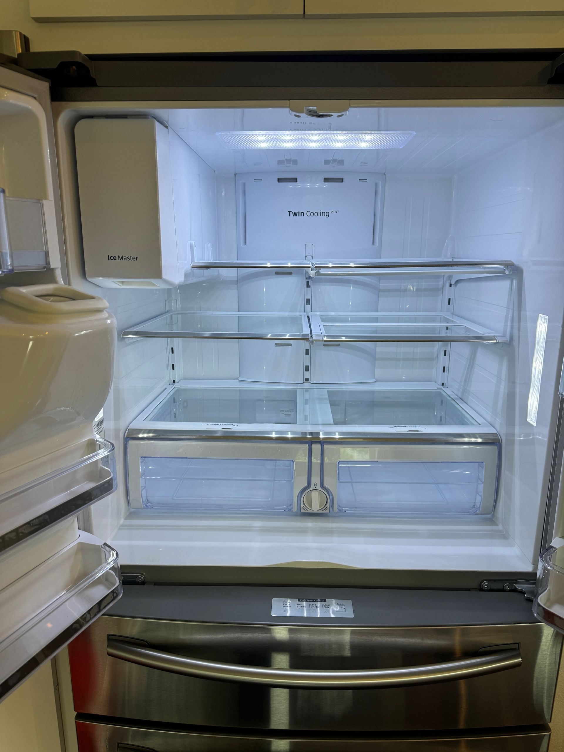 Inside of a stainless steel refrigerator with bright interior lighting. The open doors reveal glass shelves and drawers.