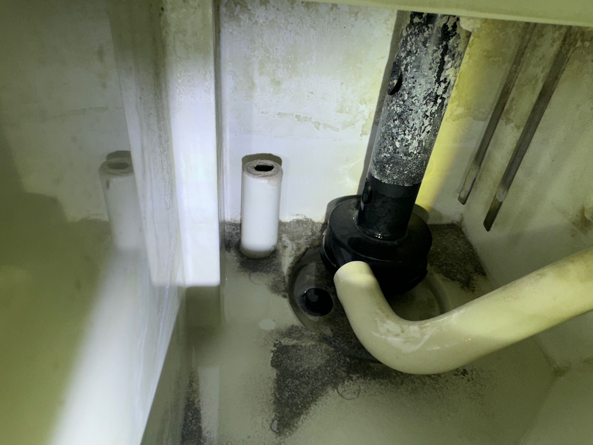 Inside of a white appliance with a pipe and various tubes; the bottom has some dark grime and is holding liquid.