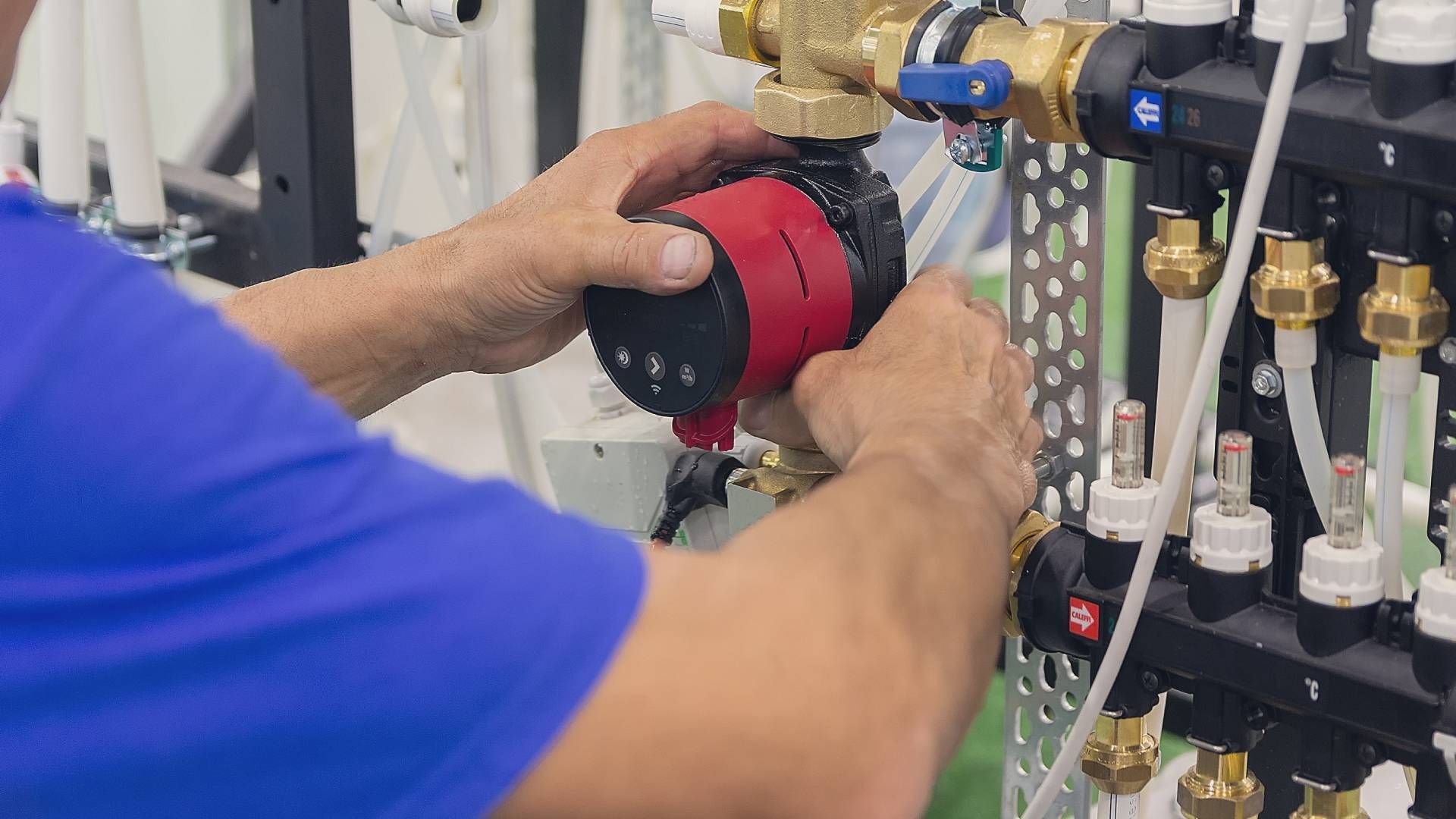 Hands of a person installing a red and black pump onto plumbing fixtures.