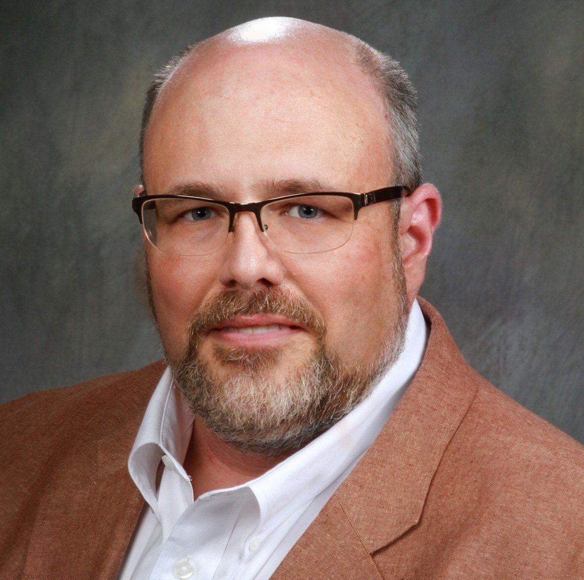 a bald man with a beard wearing glasses and a brown jacket